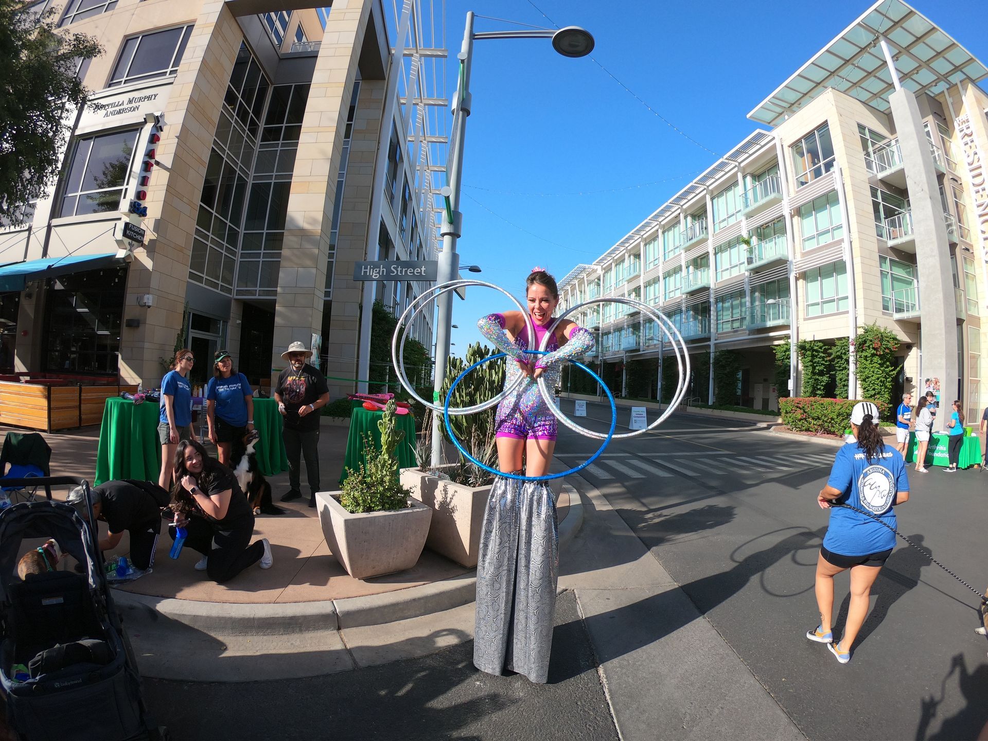 A woman is standing on stilts with hula hoops in front of a building.