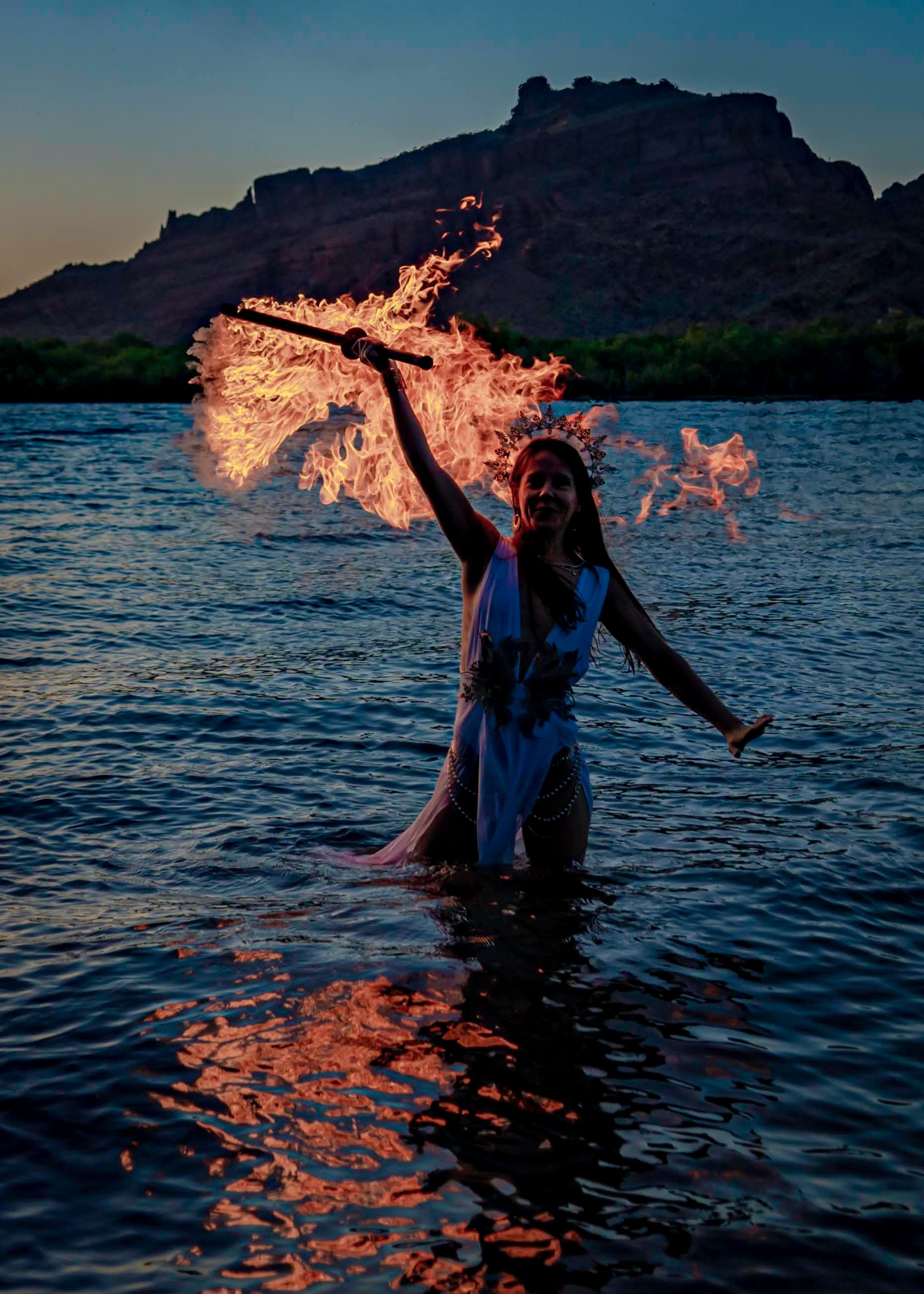 A woman is standing in the water holding a stick of fire.