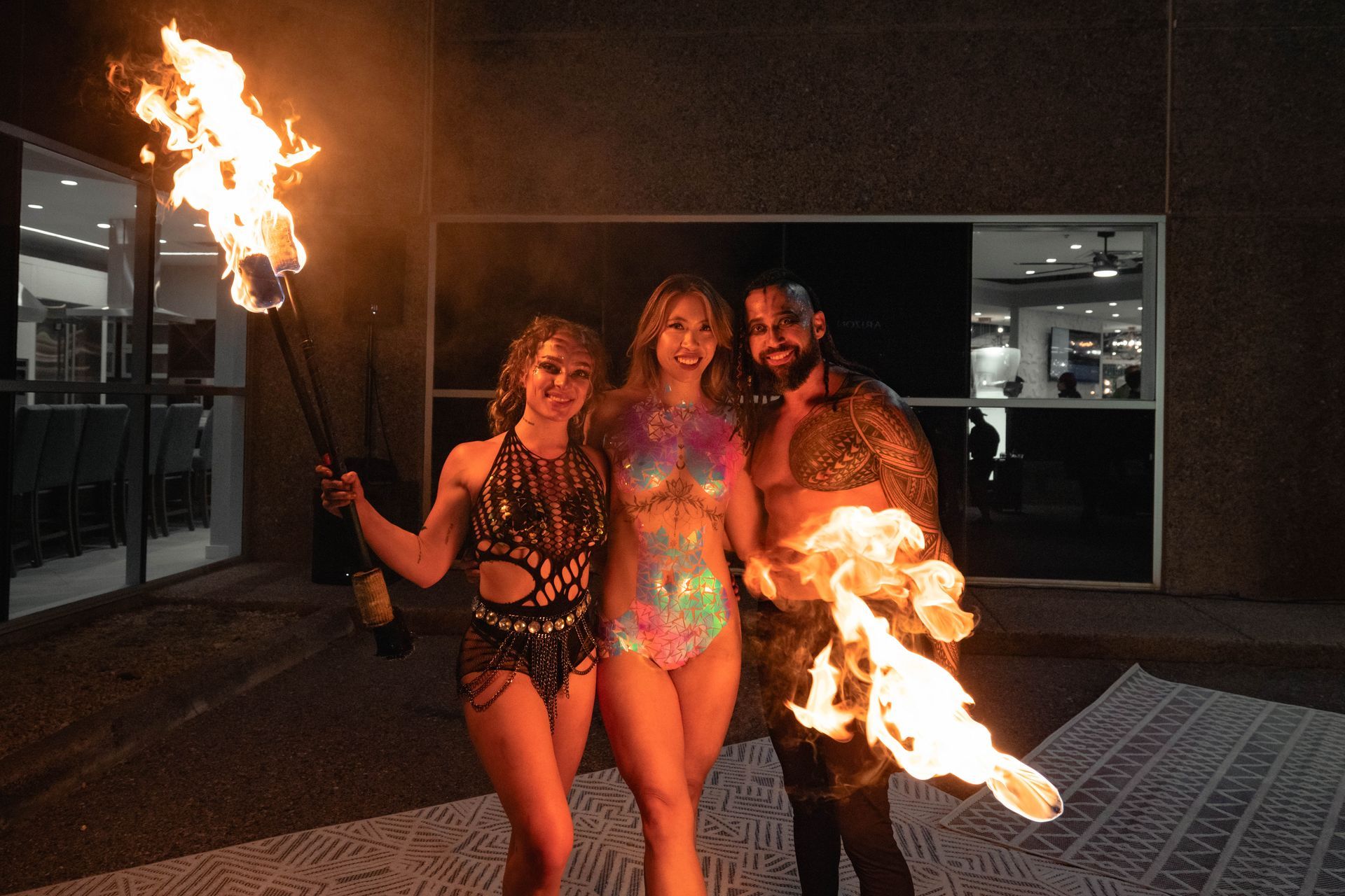 A man and two women are holding flaming torches in front of a building.