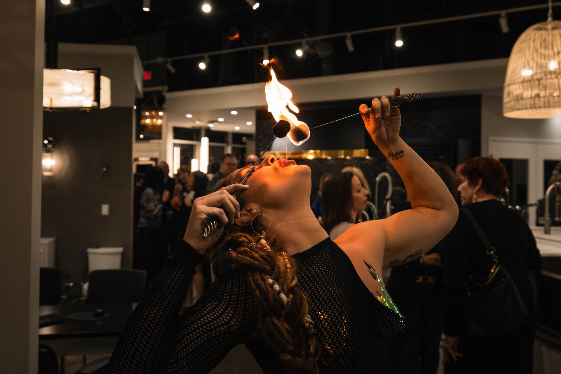 A woman is blowing fire into her mouth at a party.