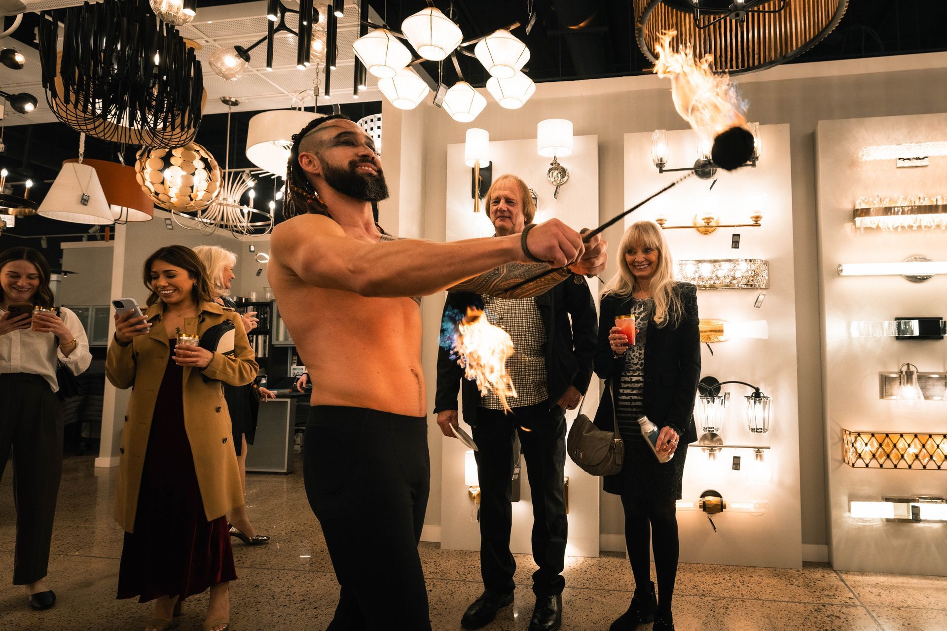 A shirtless man is holding a stick with flames coming out of it.