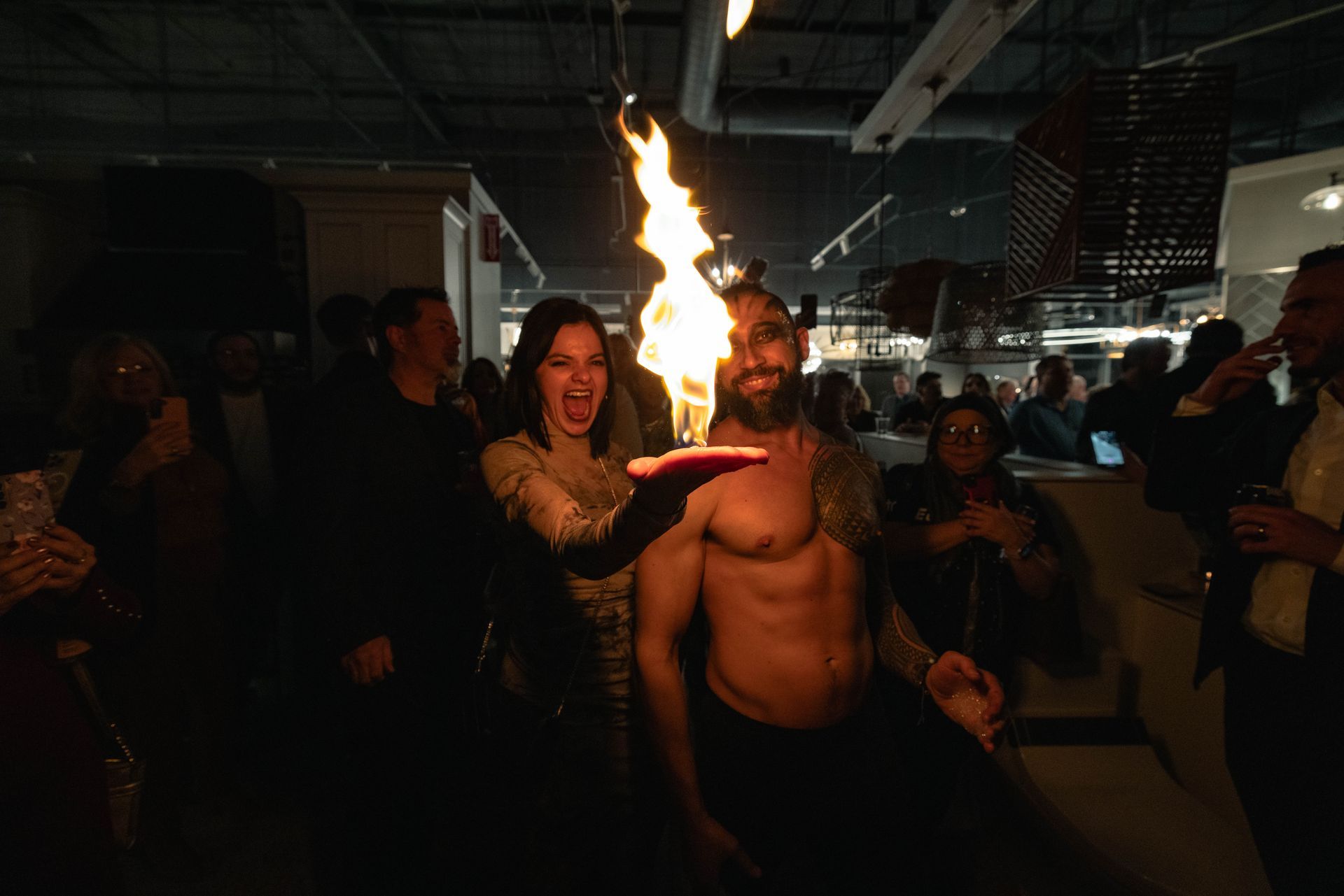 A man without a shirt is holding a torch in front of a crowd of people.