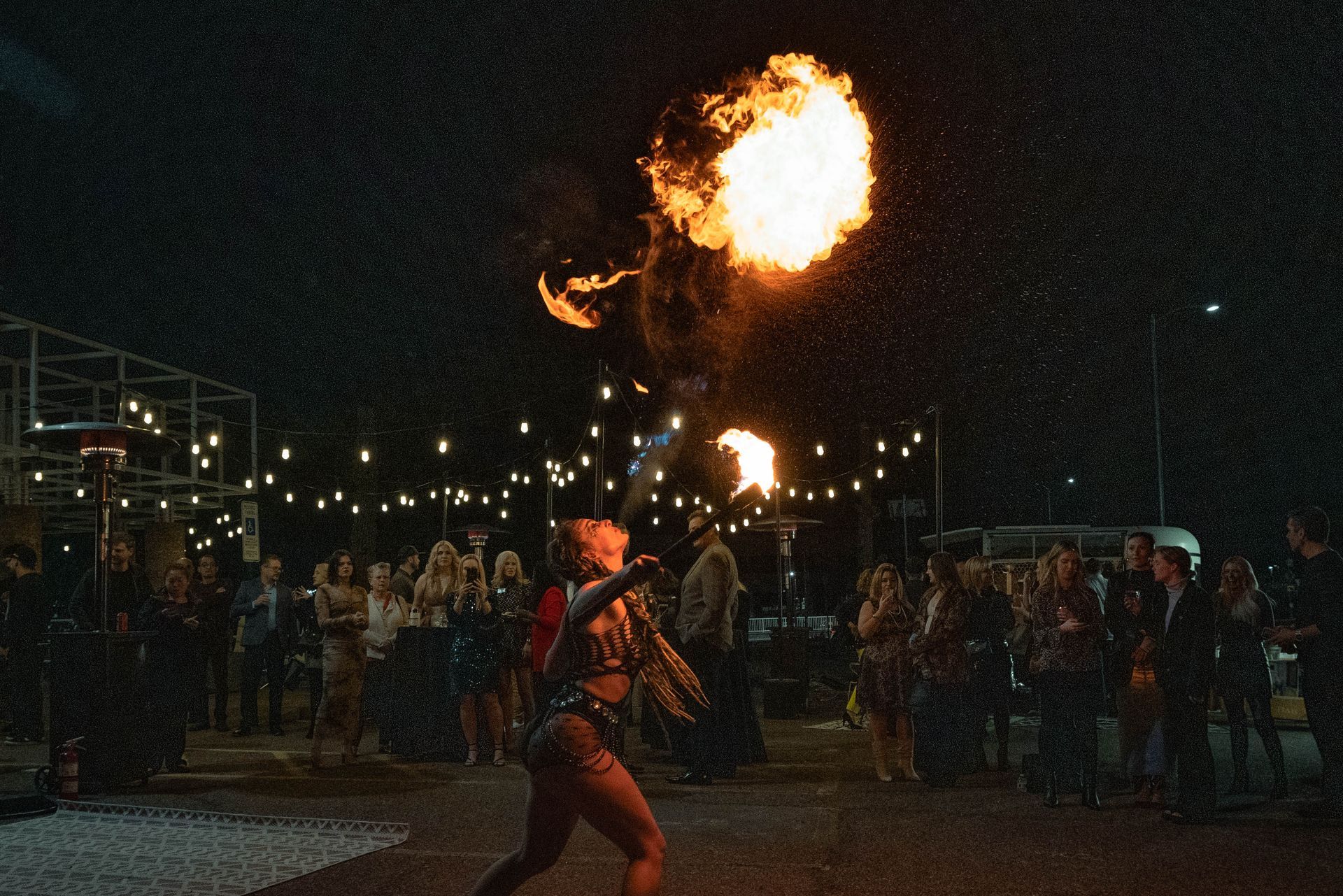 A woman is holding a fireball in front of a crowd at night.