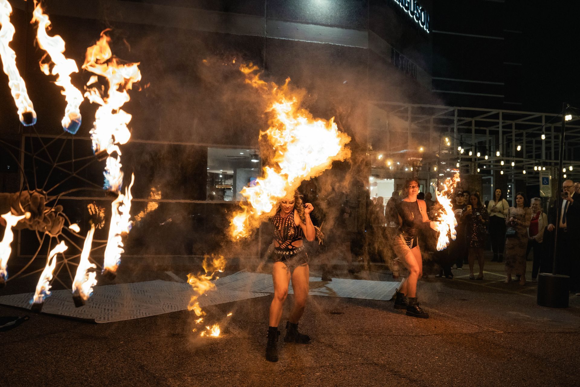 Two women are dancing with fire in their hands in front of a building.