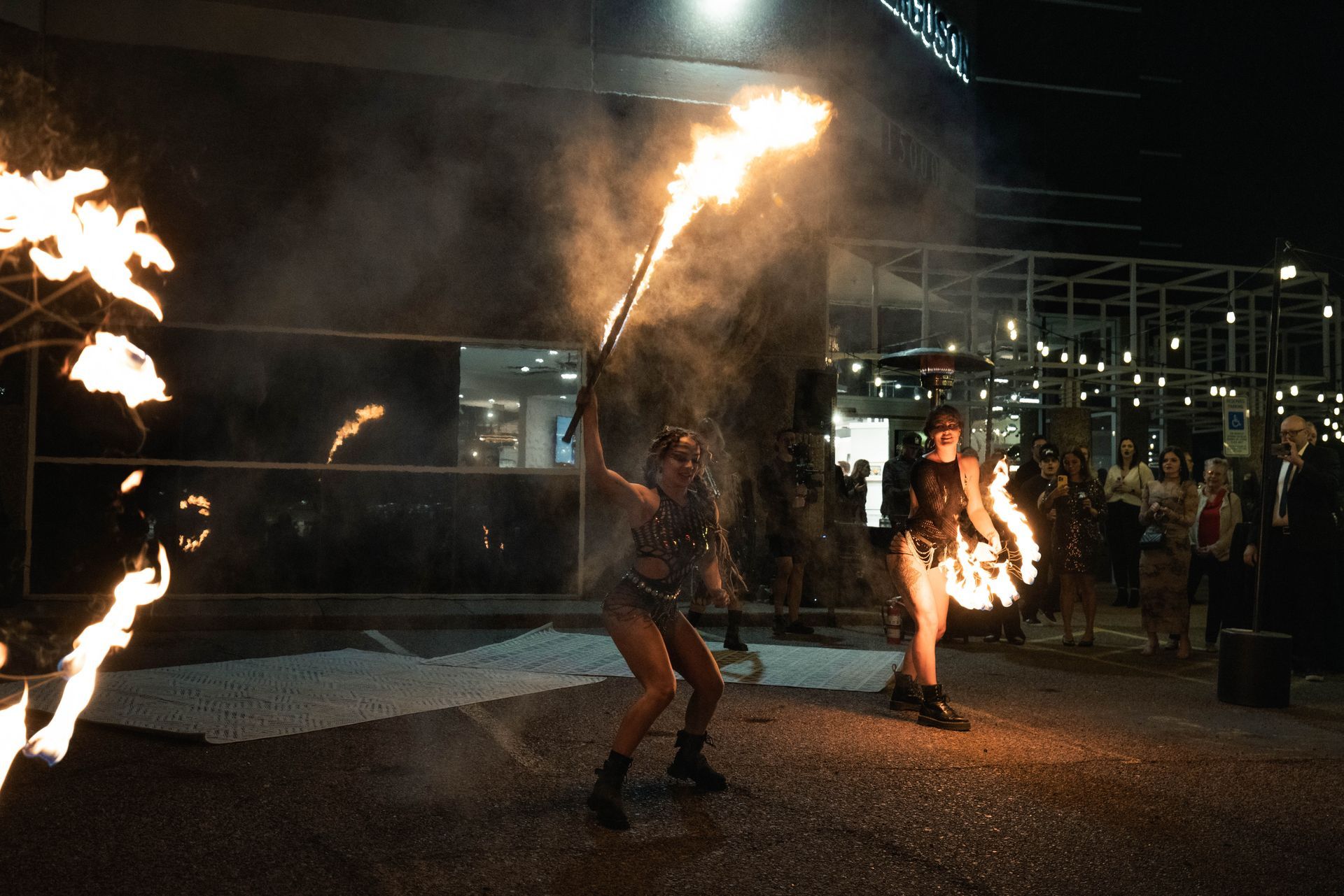 Two women are holding flaming torches in front of a building at night.