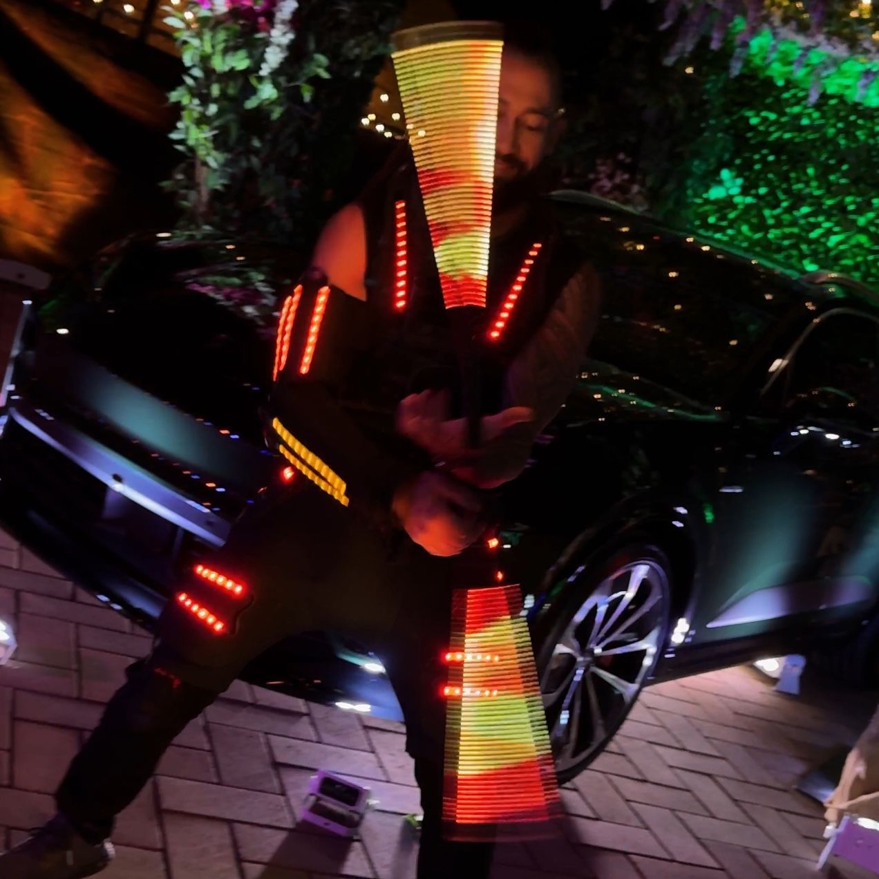 A man in a costume with lights on his arms is standing in front of a car