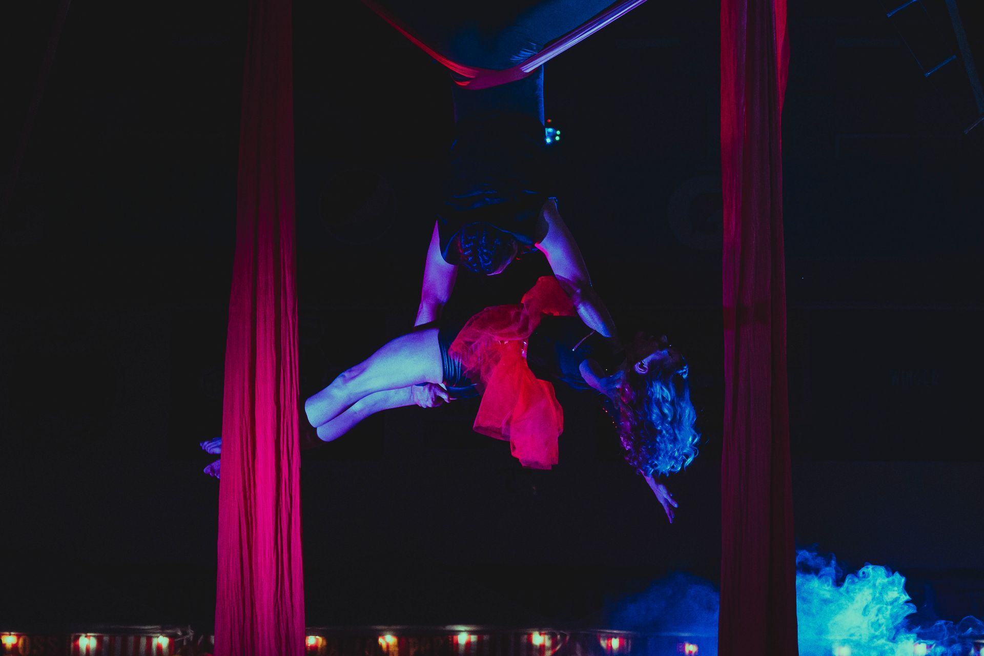 A woman is performing aerial acrobatics on a red curtain in a dark room.