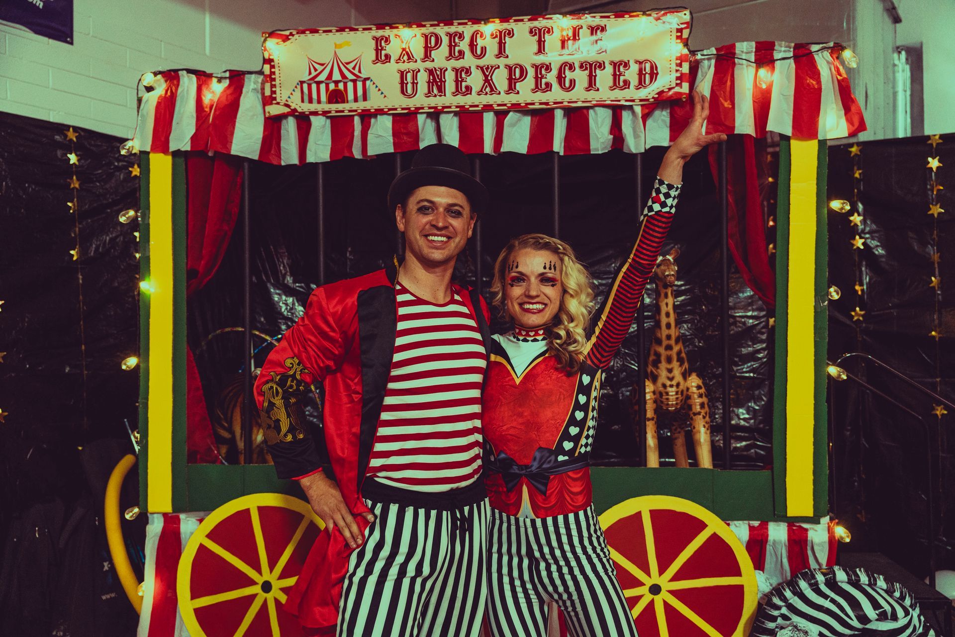 A man and a woman are posing for a picture in front of a sign that says expect the unexpected.