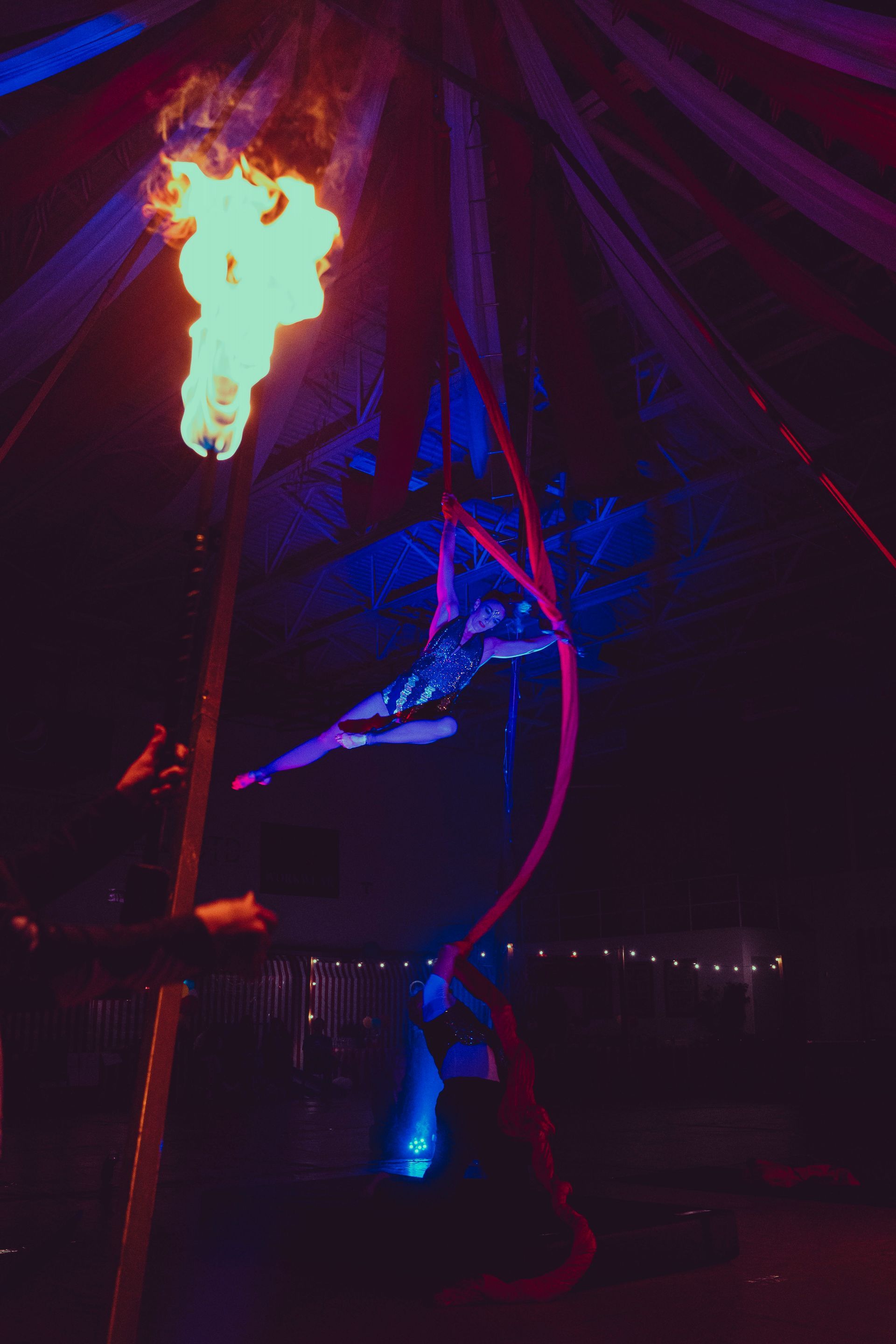 A woman is performing aerial acrobatics in a tent with a fire torch.