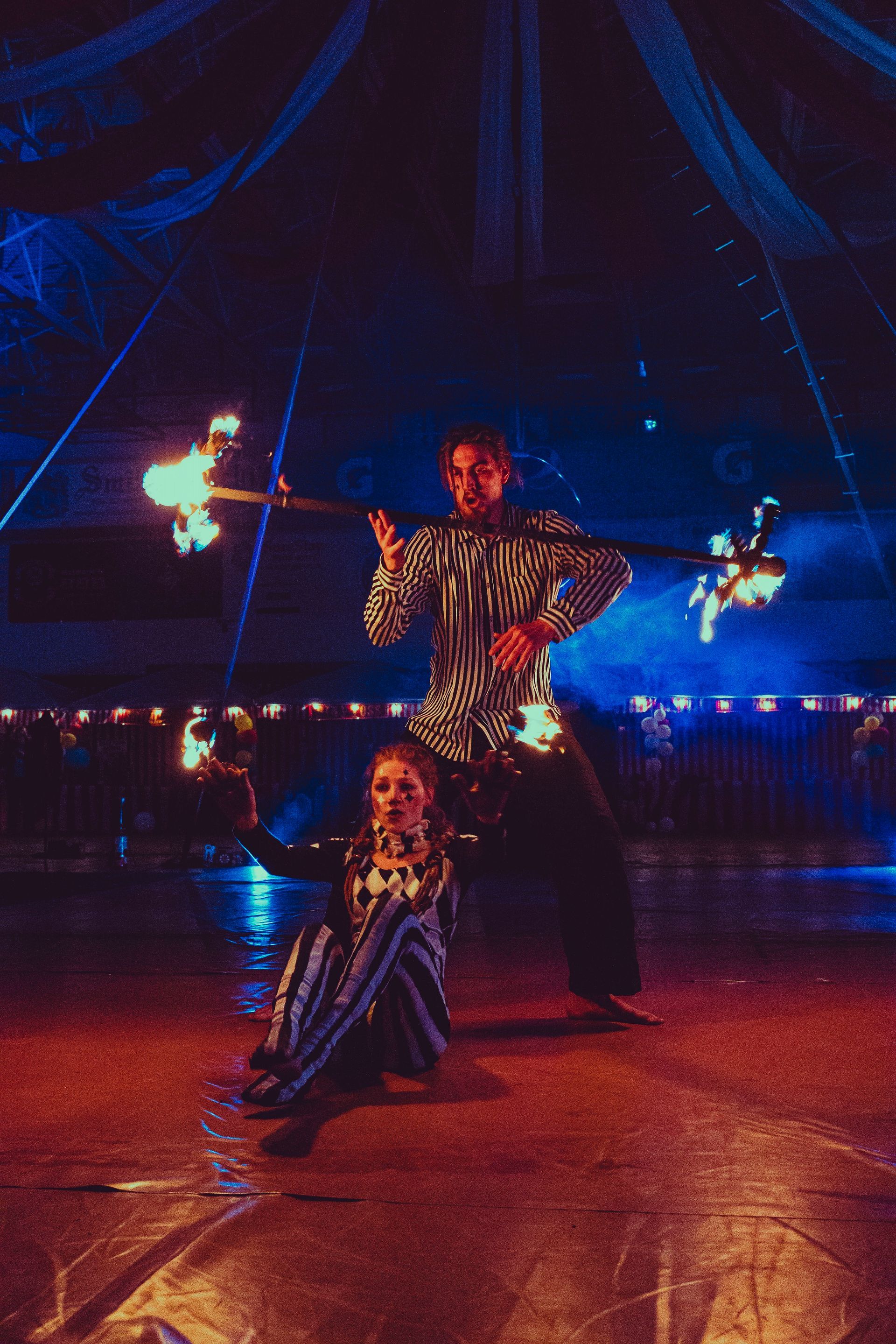 A man and a woman are dancing with fire in a circus tent.