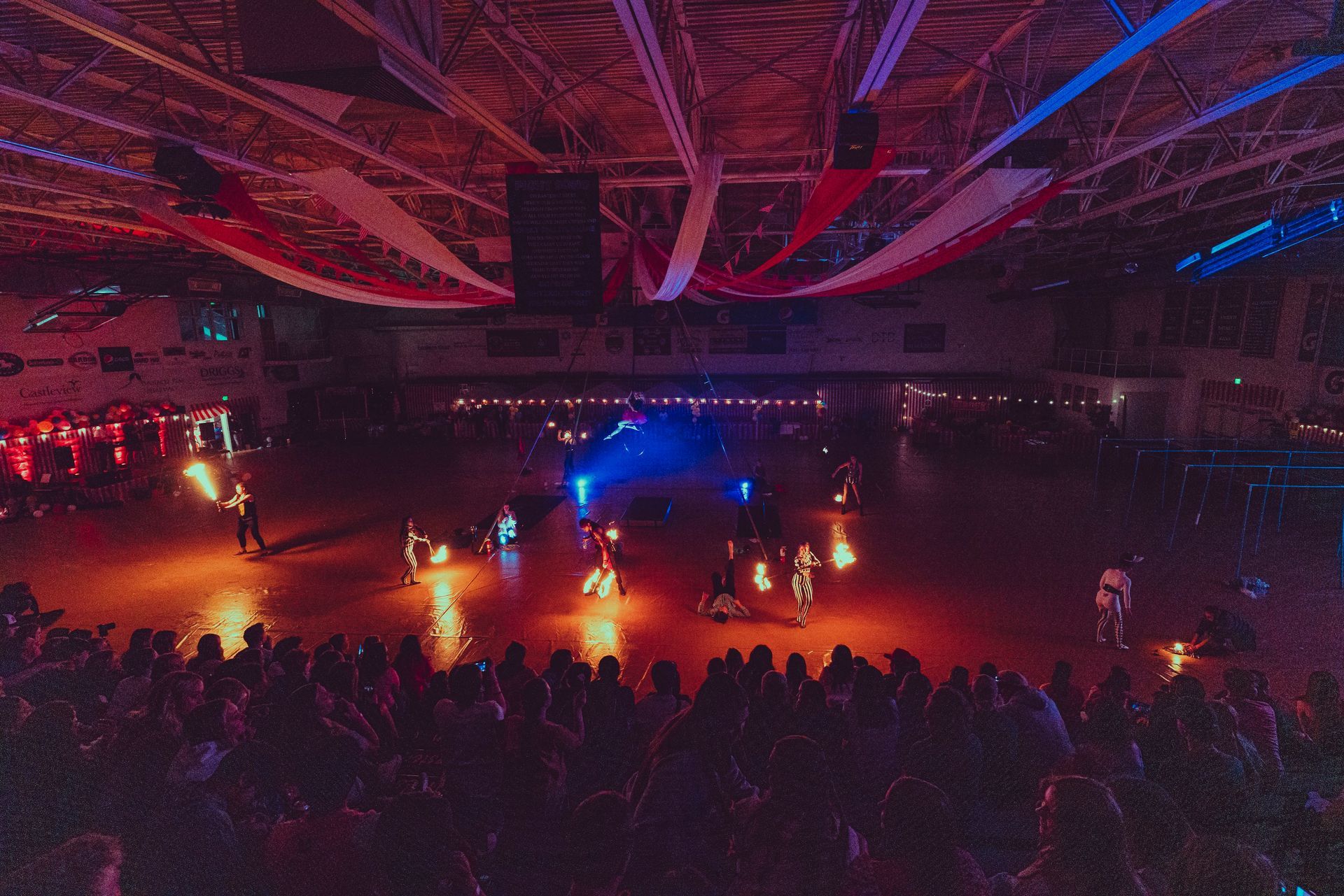 A crowd of people are watching a fire show in a large indoor arena.