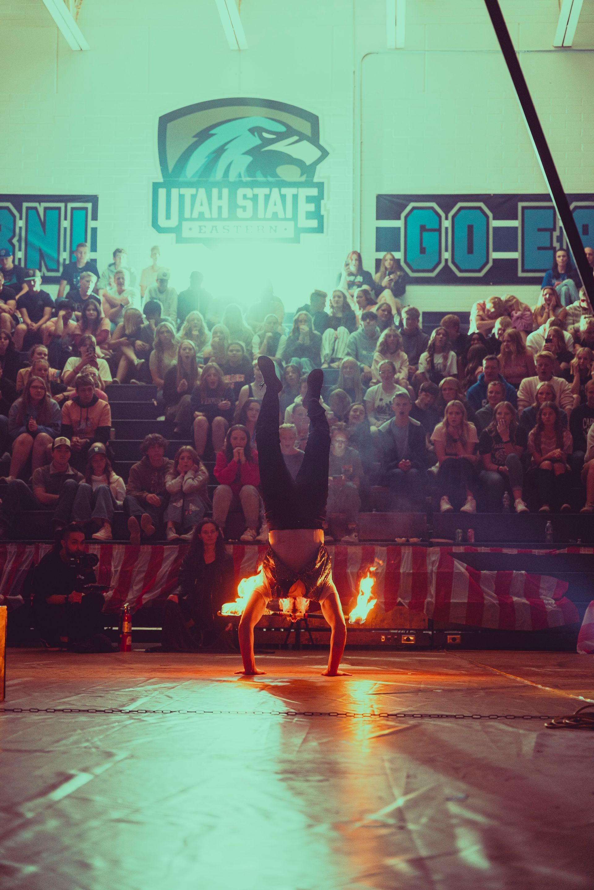 A man is doing a handstand on a basketball court in front of a crowd.