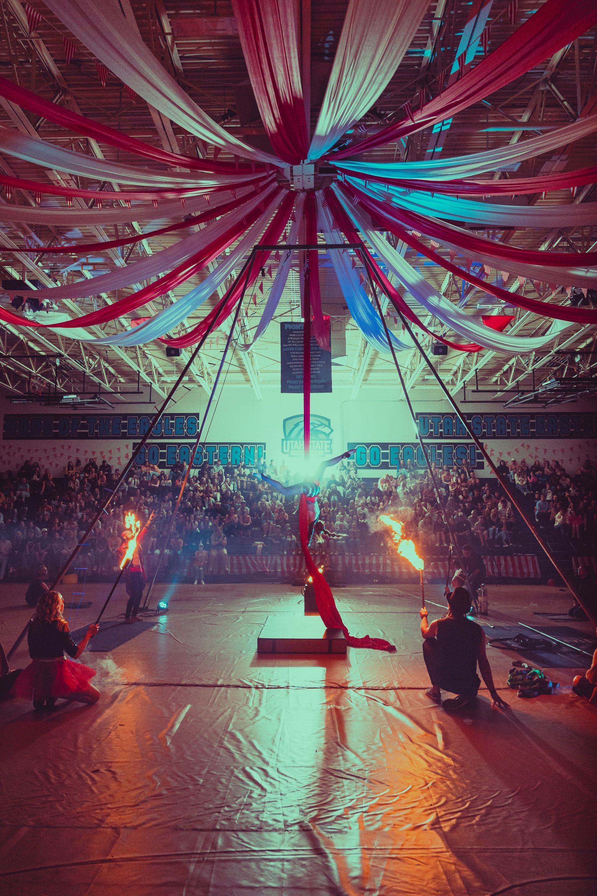 A group of people are performing aerial acrobatics in front of a crowd in a gym.