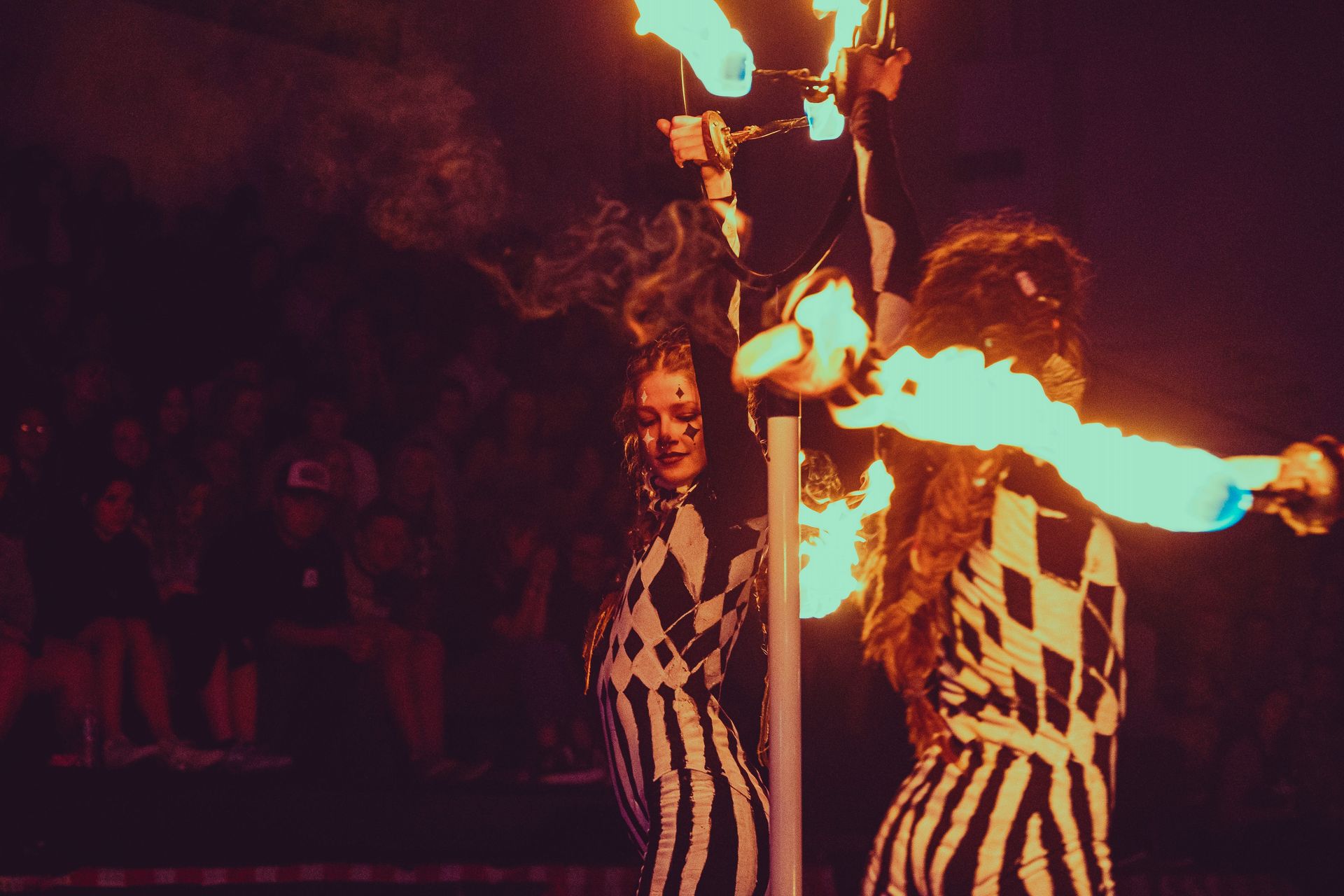 Two women in striped outfits are holding flaming torches in front of a crowd.