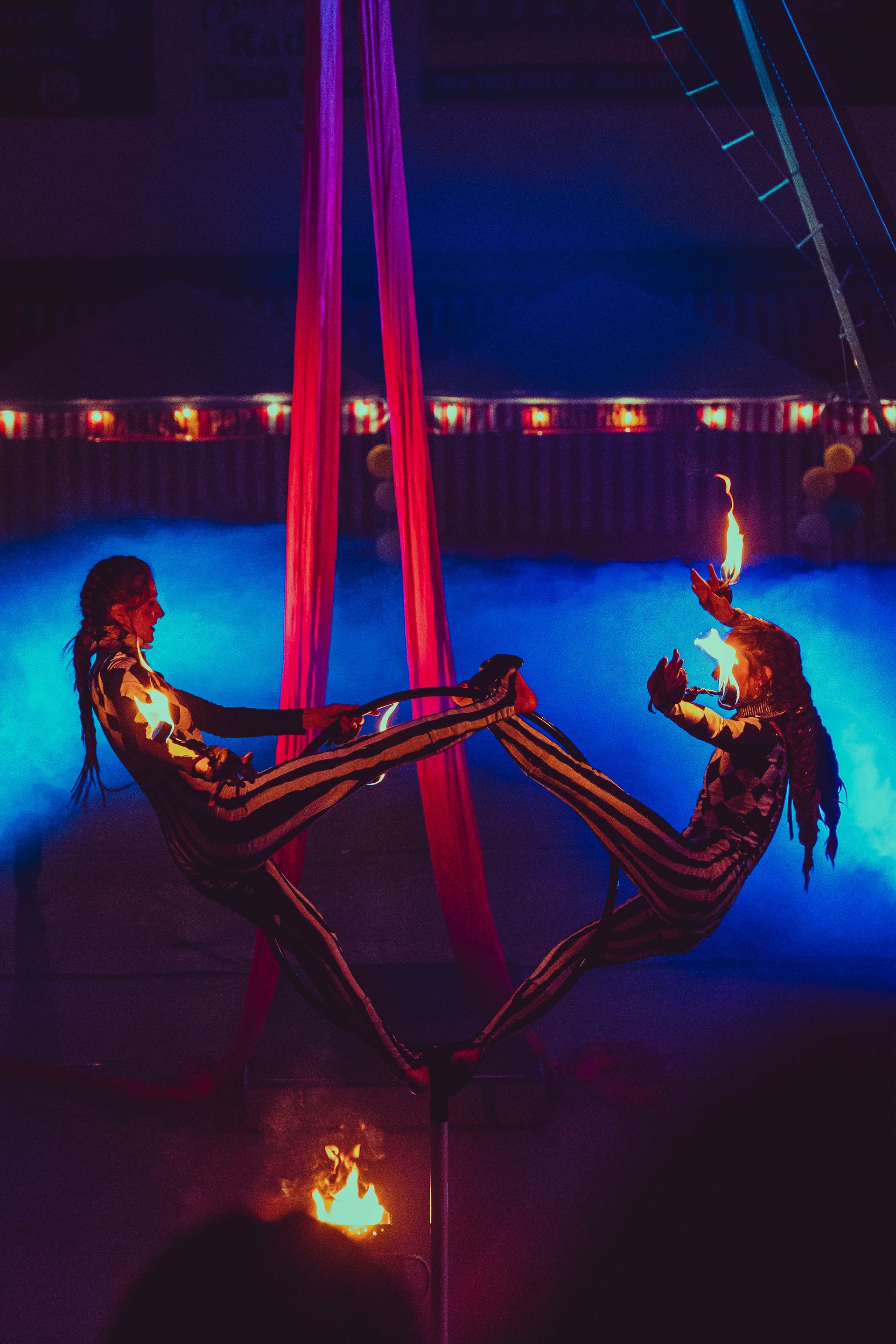 Two aerial acrobats are performing aerial tricks in a dark room.