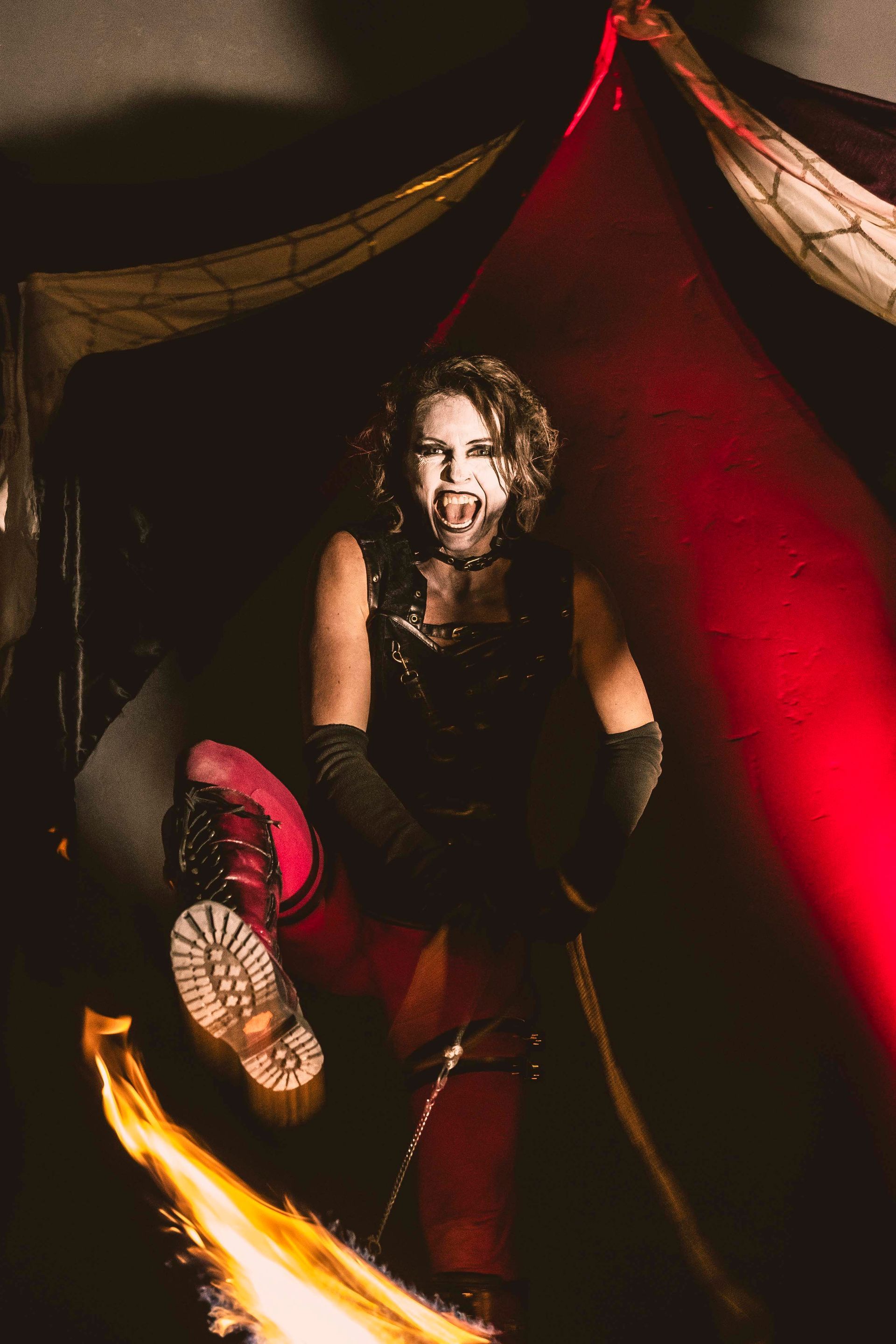 A woman in a vampire costume is sitting next to a fire.