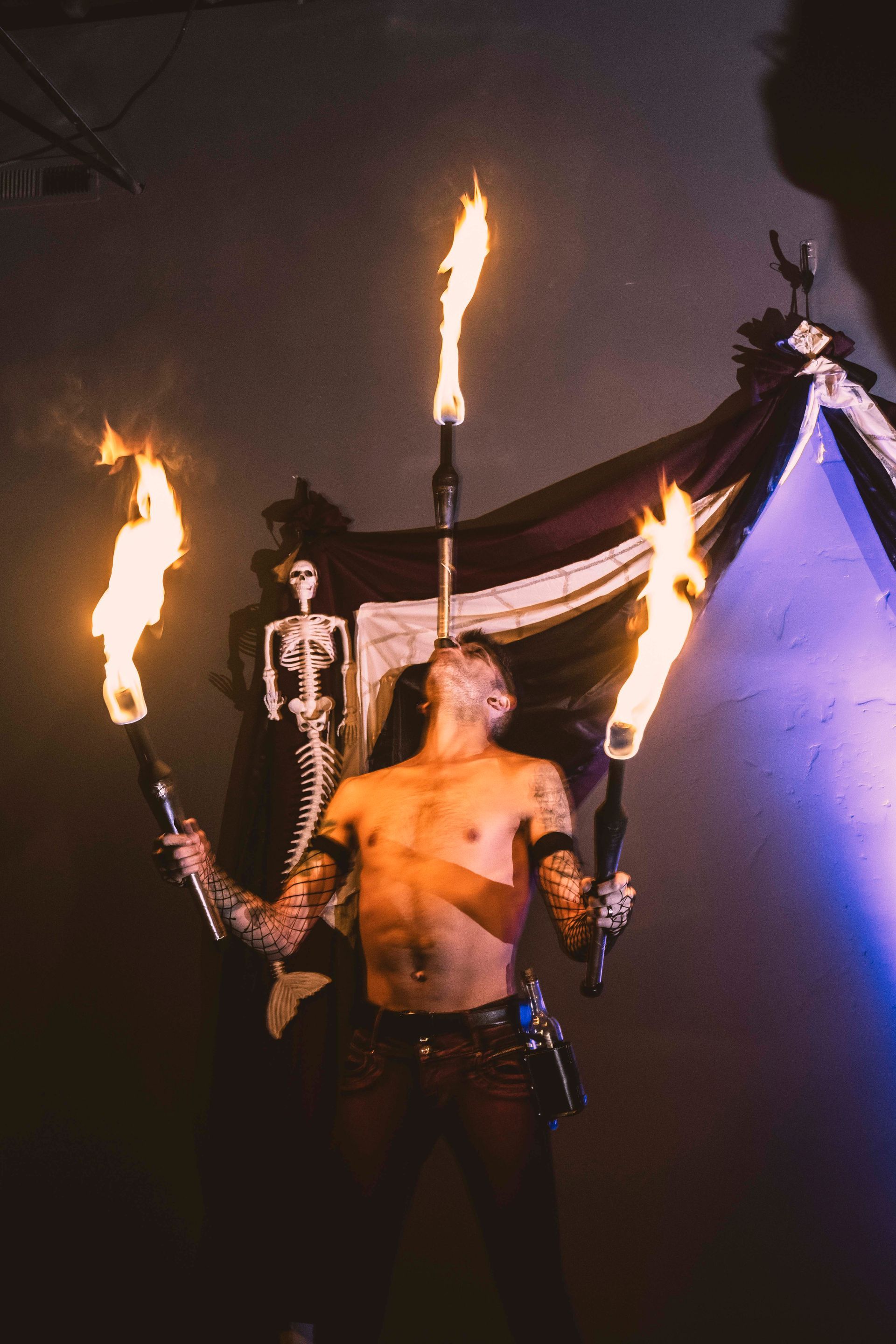 A shirtless man is holding three fire torches in front of his face.