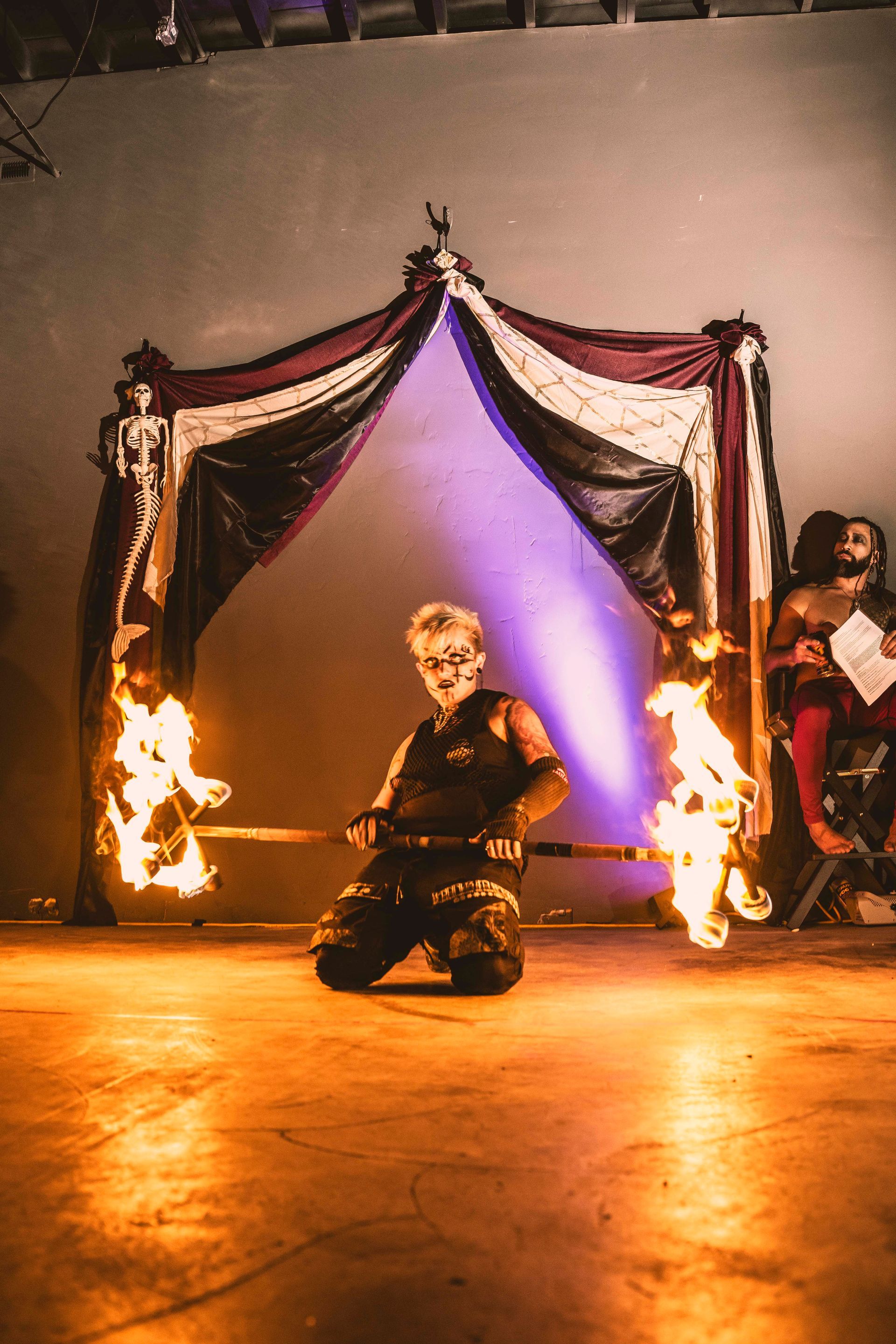 A man is kneeling down in front of a curtain with fire coming out of it.