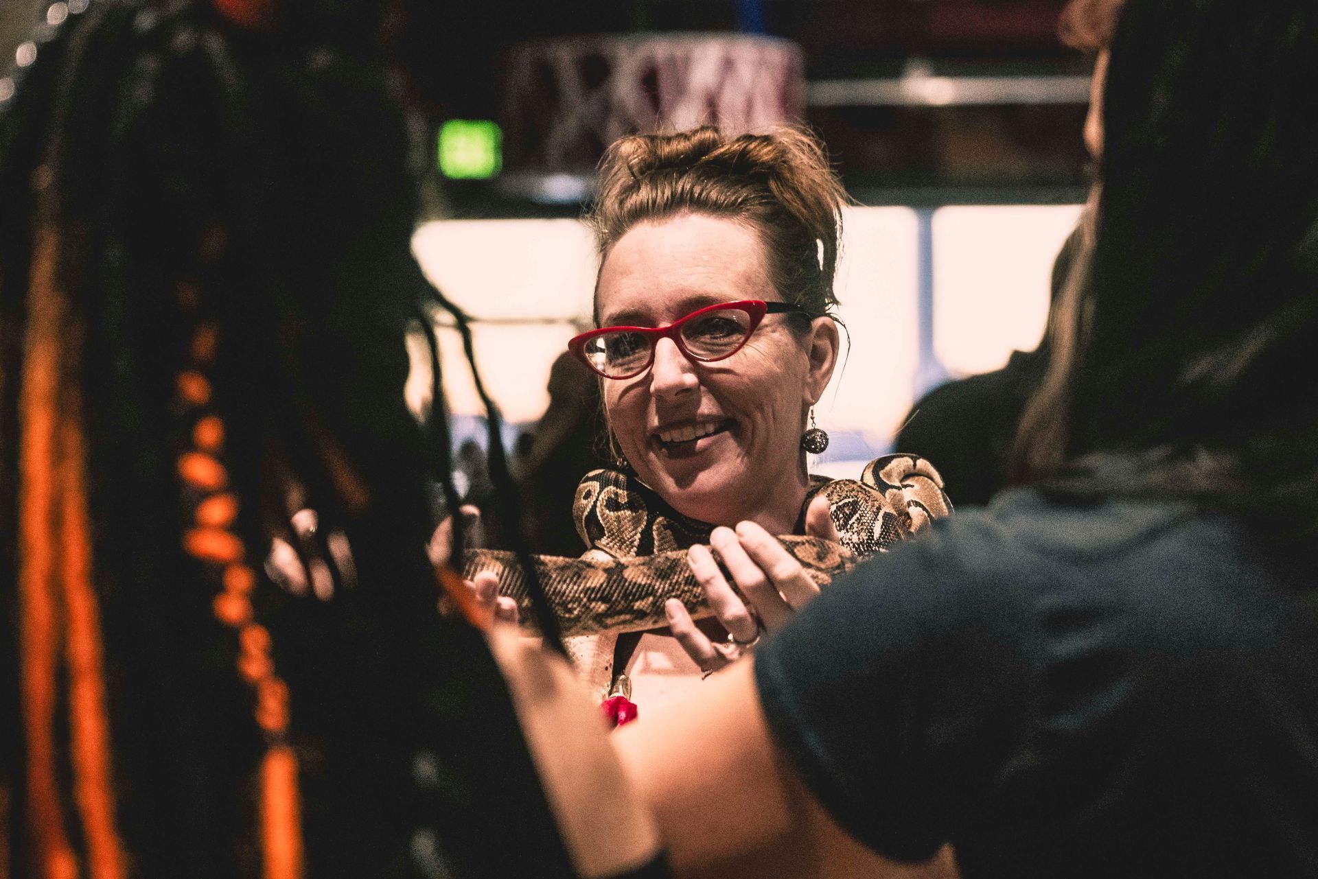 A woman wearing glasses is smiling while holding a snake.