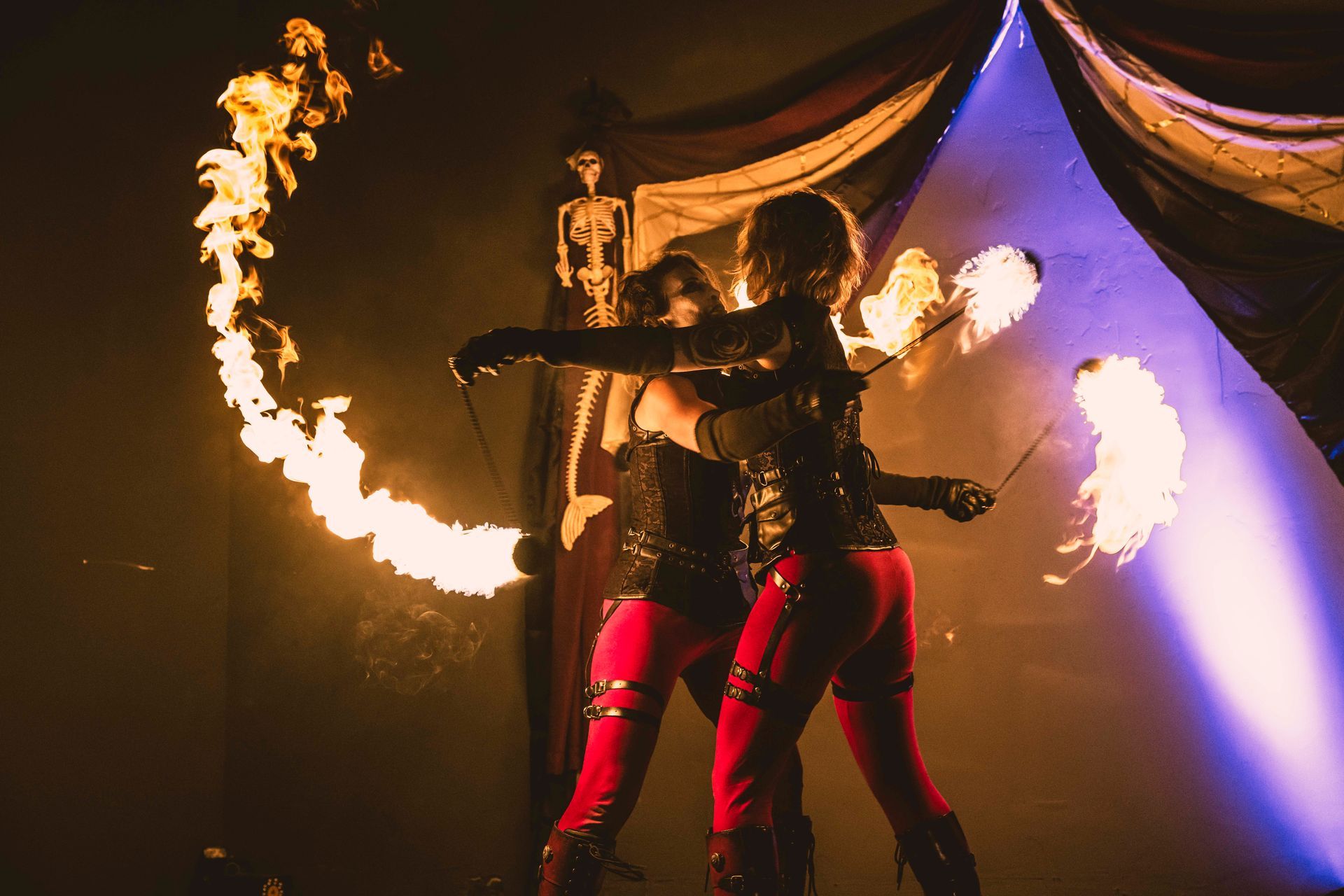 Two people are performing a fire show in a dark room.