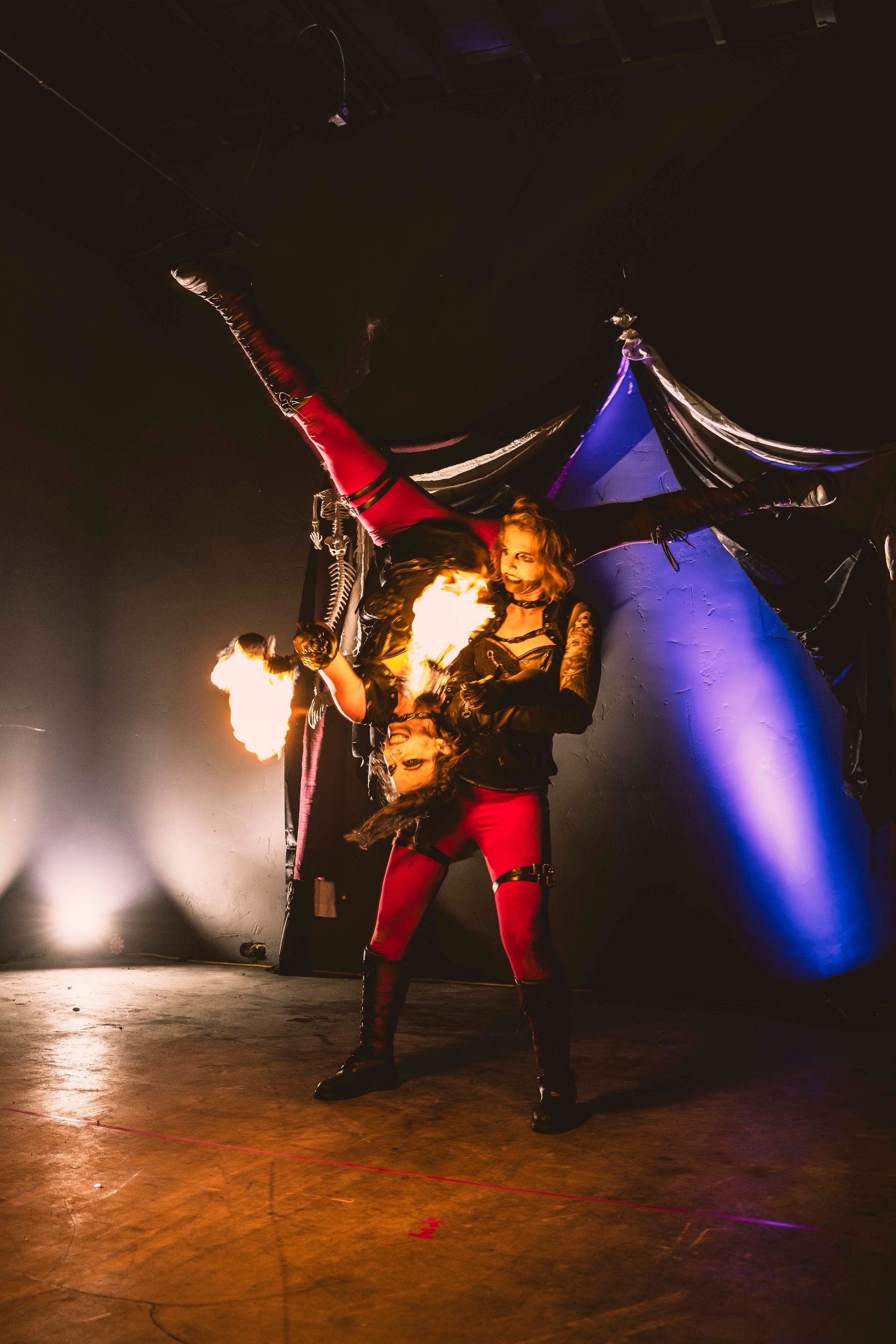 A woman in a devil costume is holding a fire torch in a dark room.