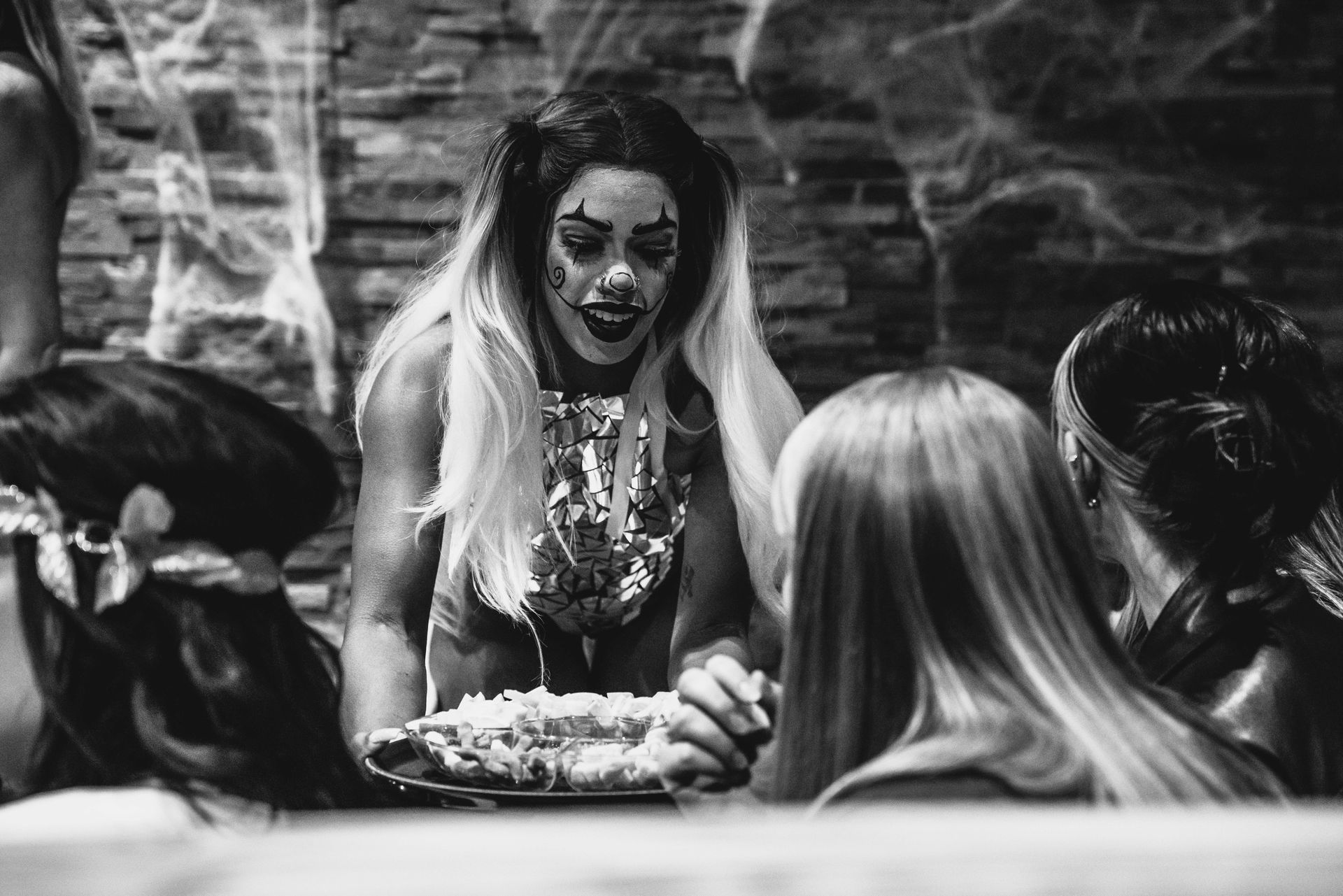 A woman in a clown costume is blowing out candles on a birthday cake.
