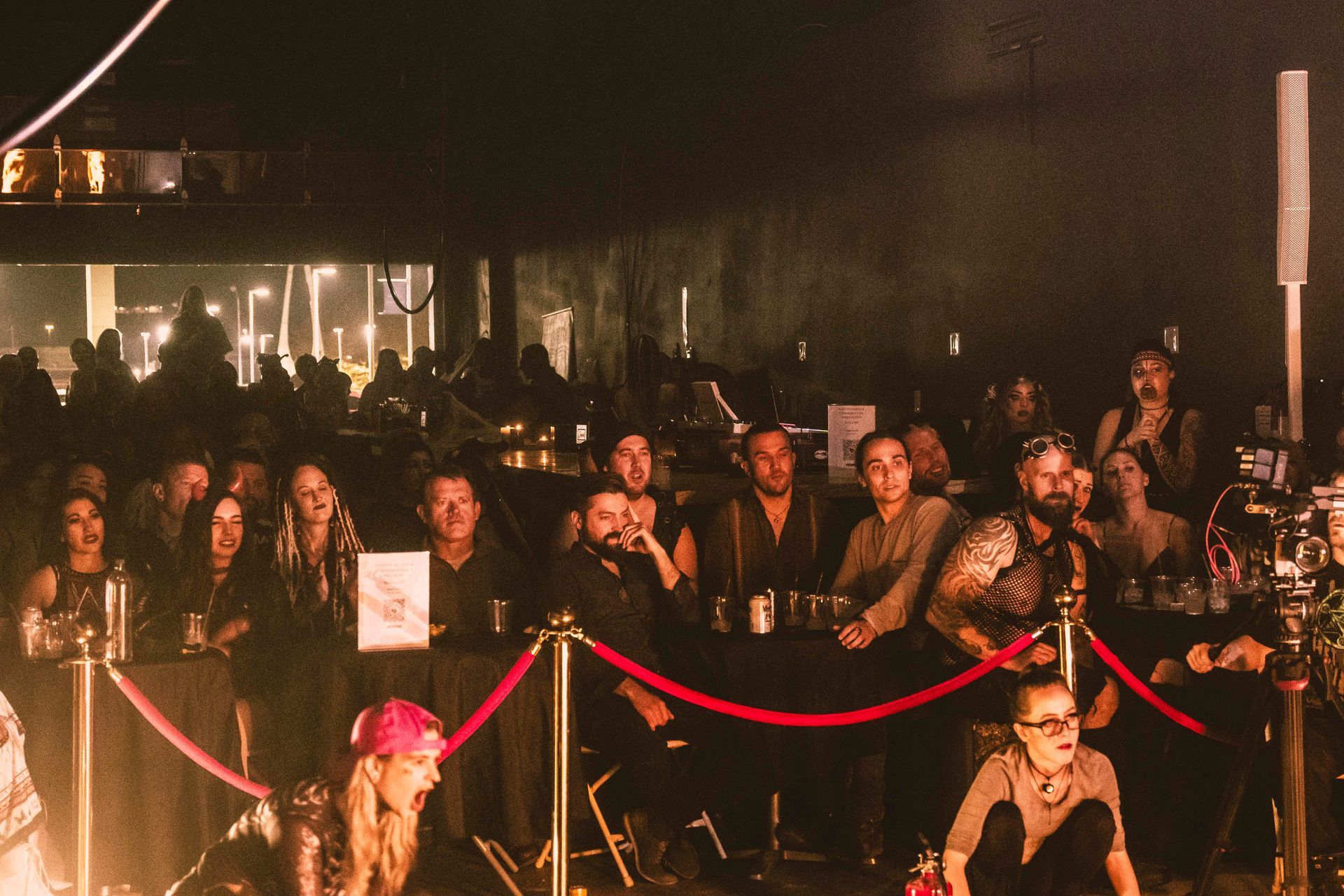 A crowd of people are sitting in a dark room behind a red rope barrier.