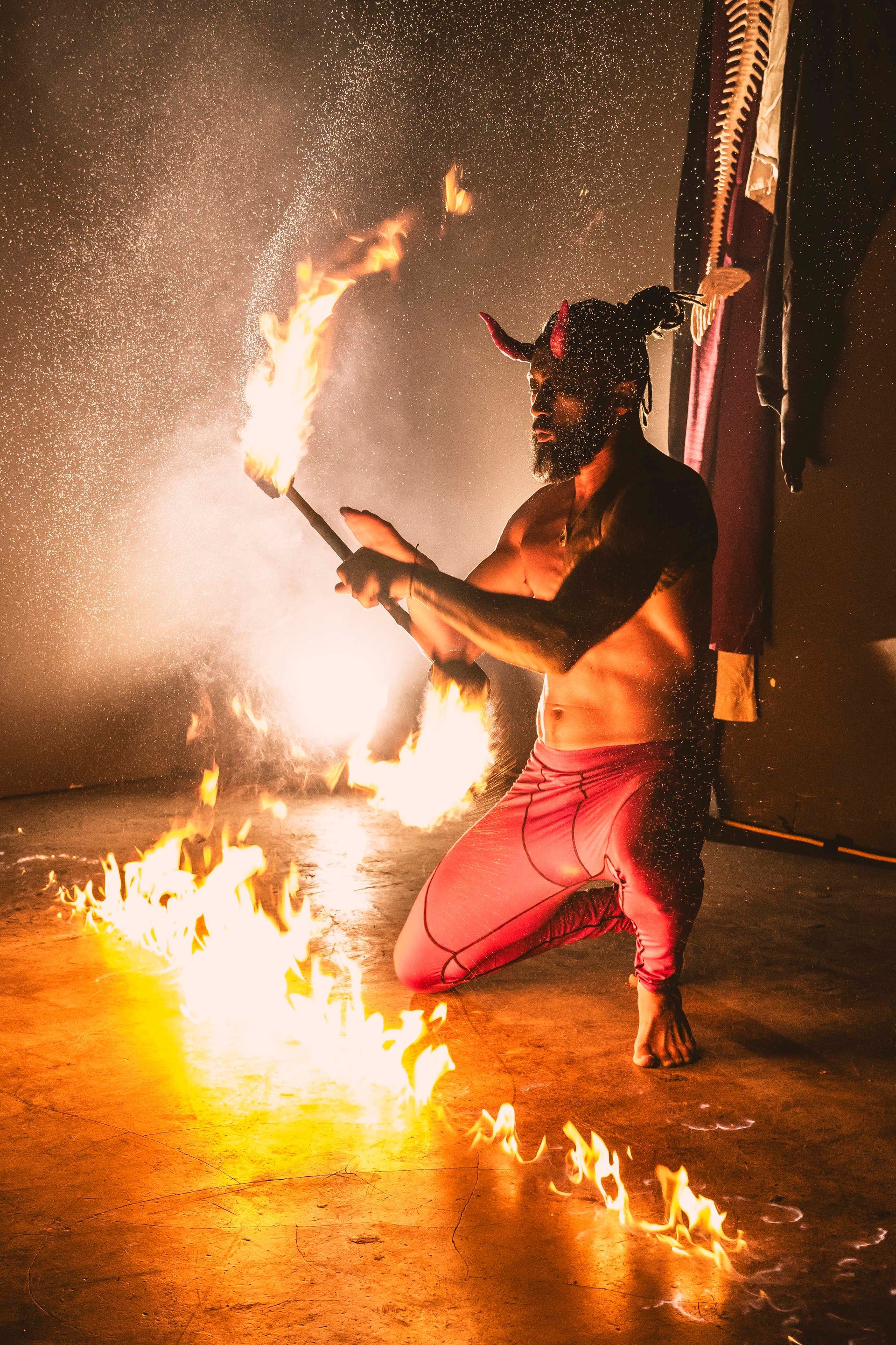 A man in a devil costume is holding a stick of fire in a dark room.