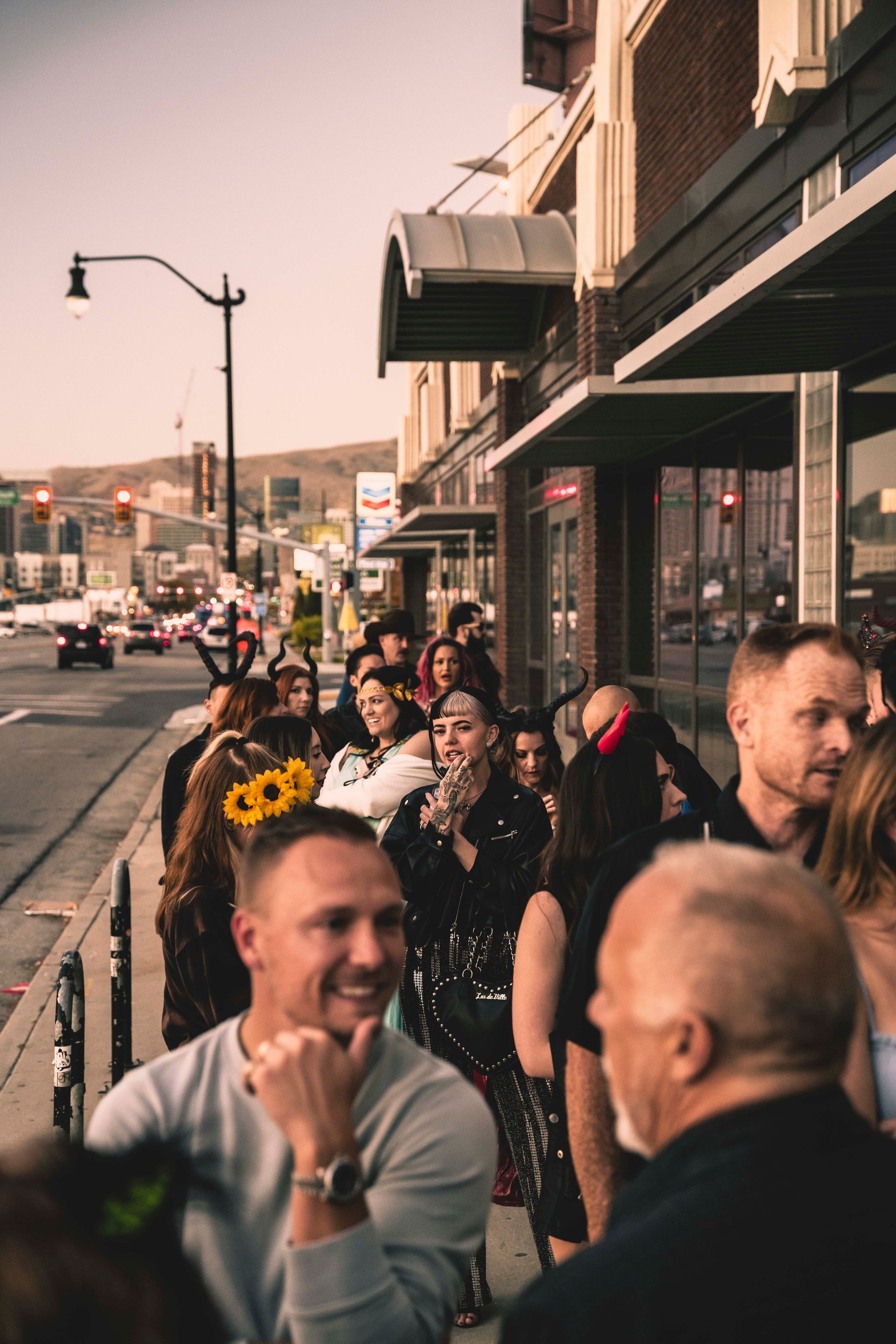 A group of people are standing on the sidewalk in front of a building.