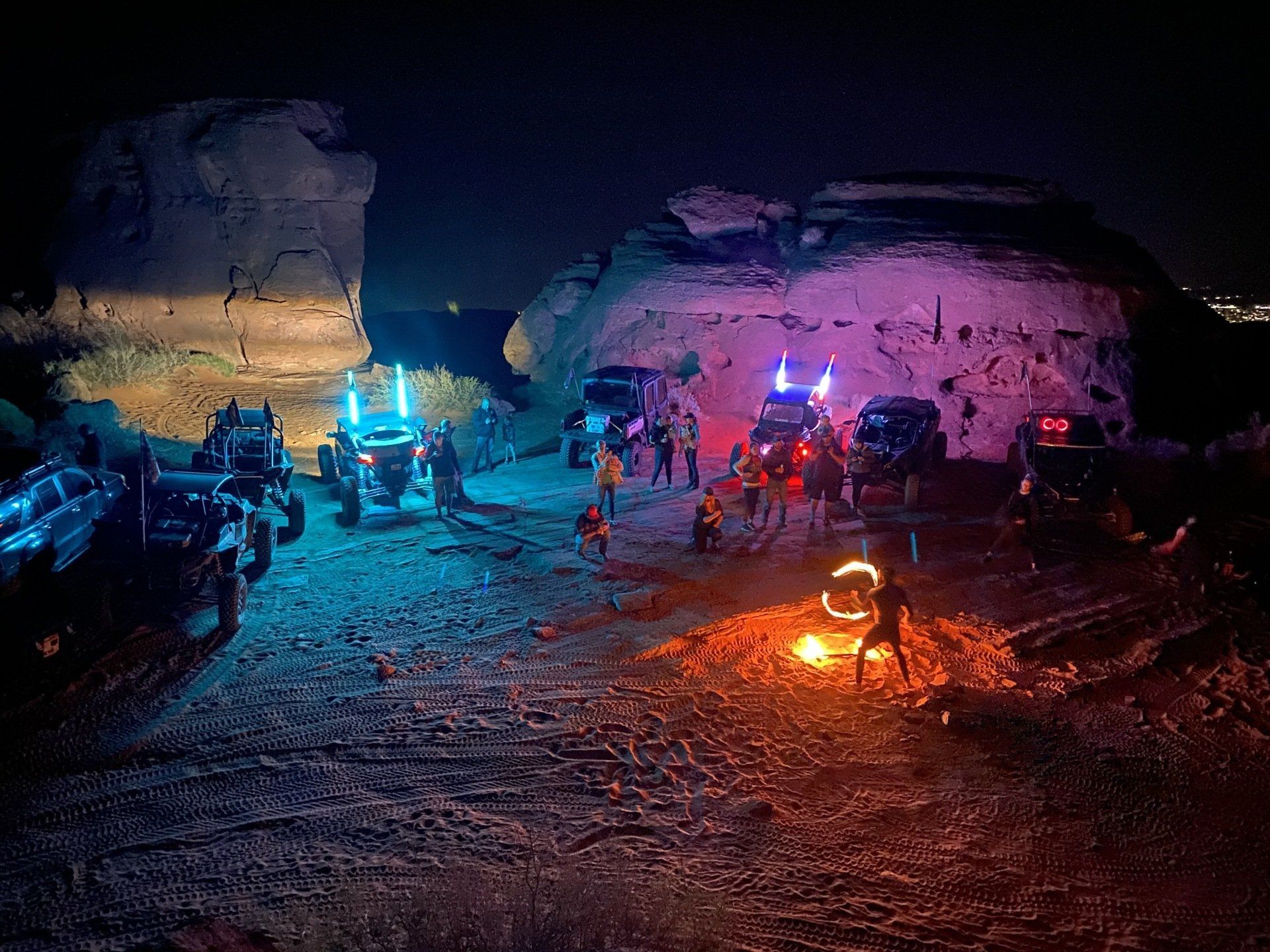 A group of people are standing around a campfire in the desert at night.