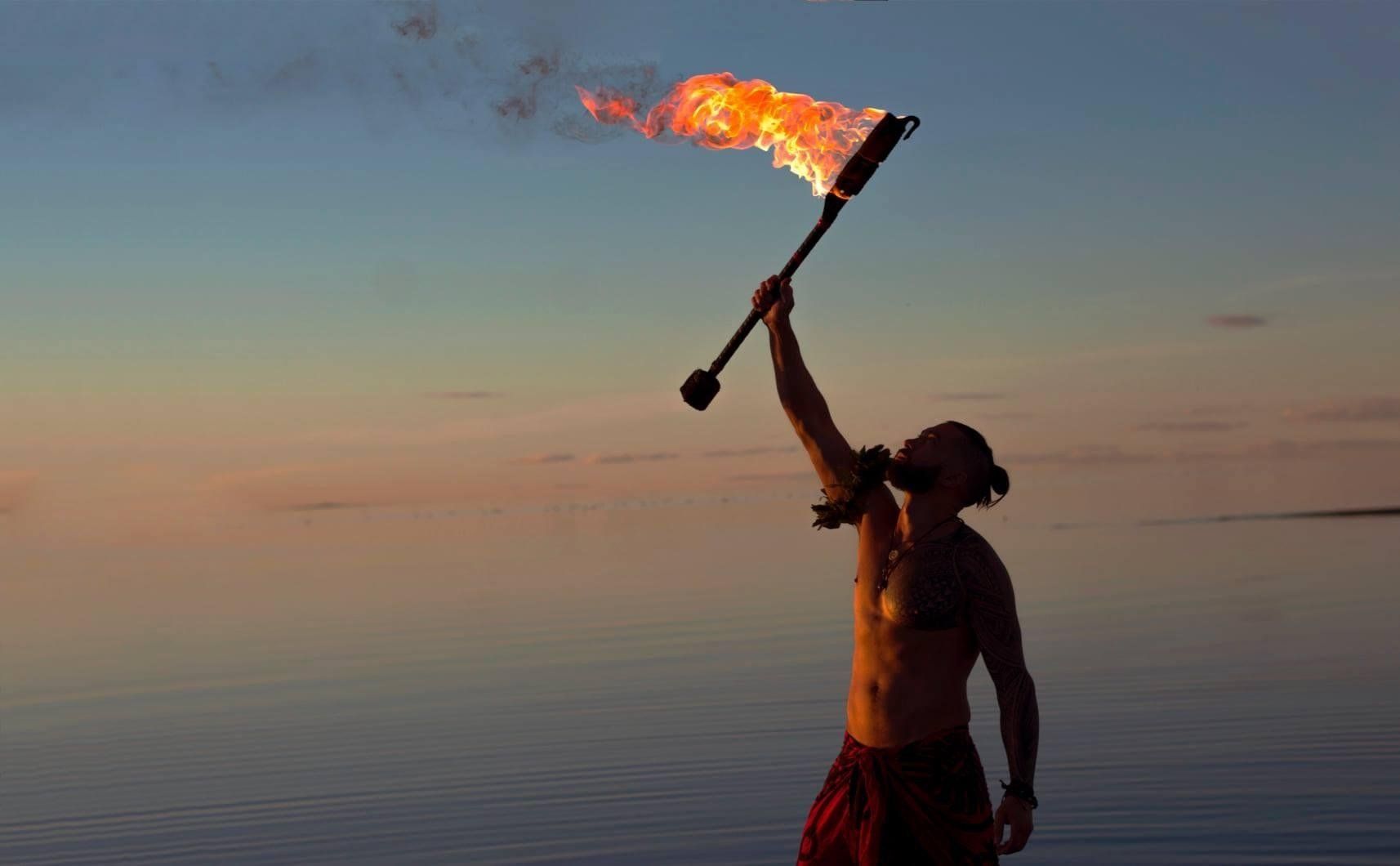 A man is holding a torch in the air on the beach.