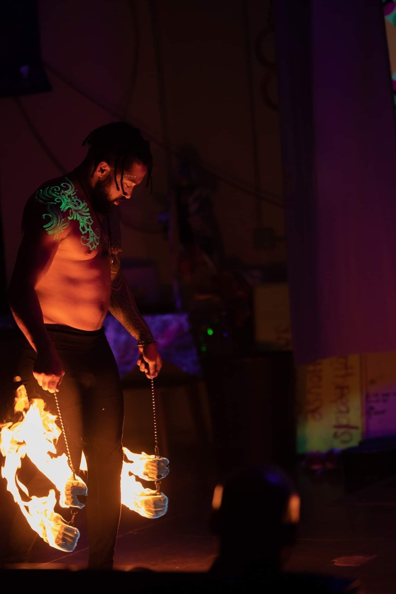 A shirtless man is holding a stick with flames on it in a dark room.