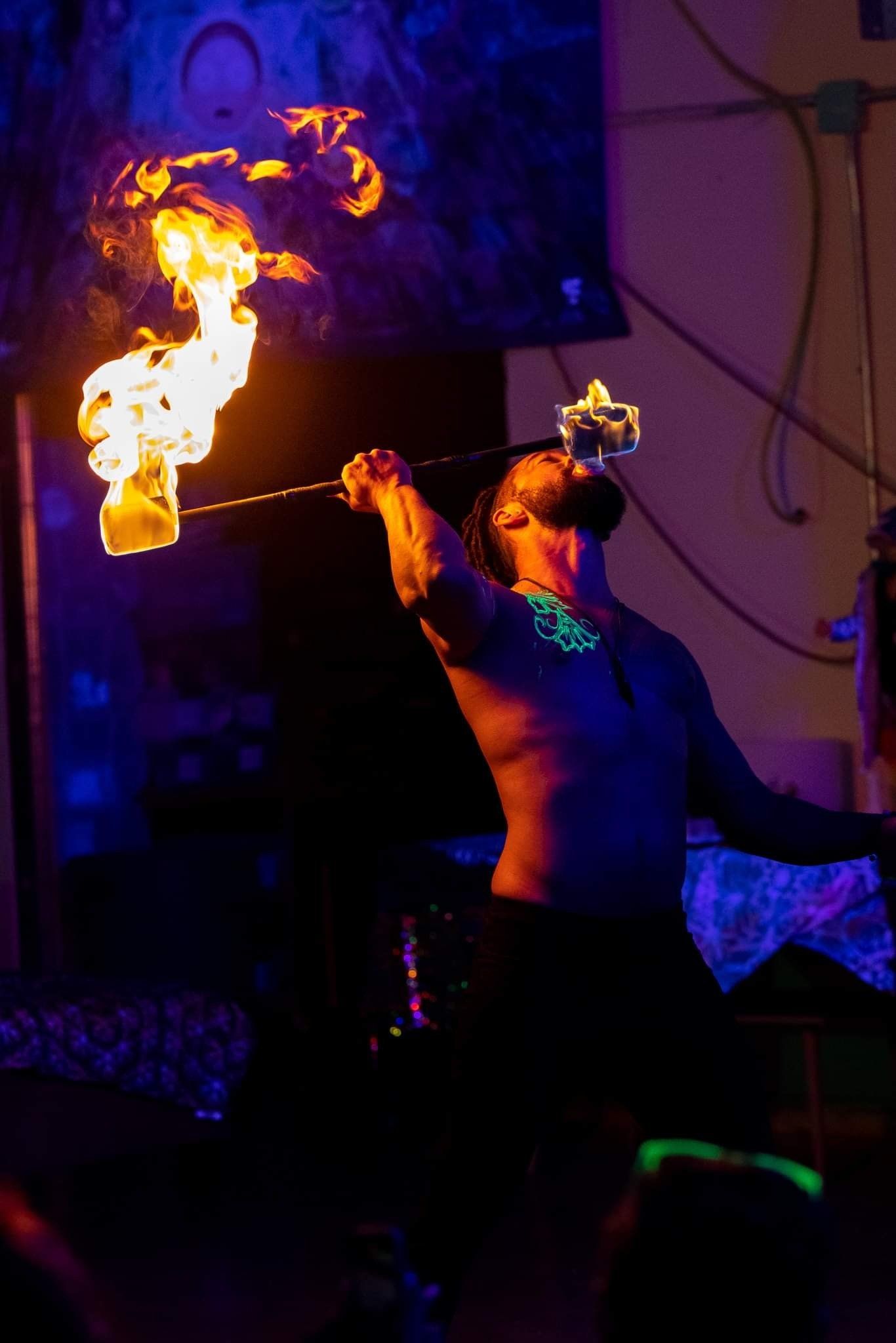 A man without a shirt is holding a torch with flames coming out of it.