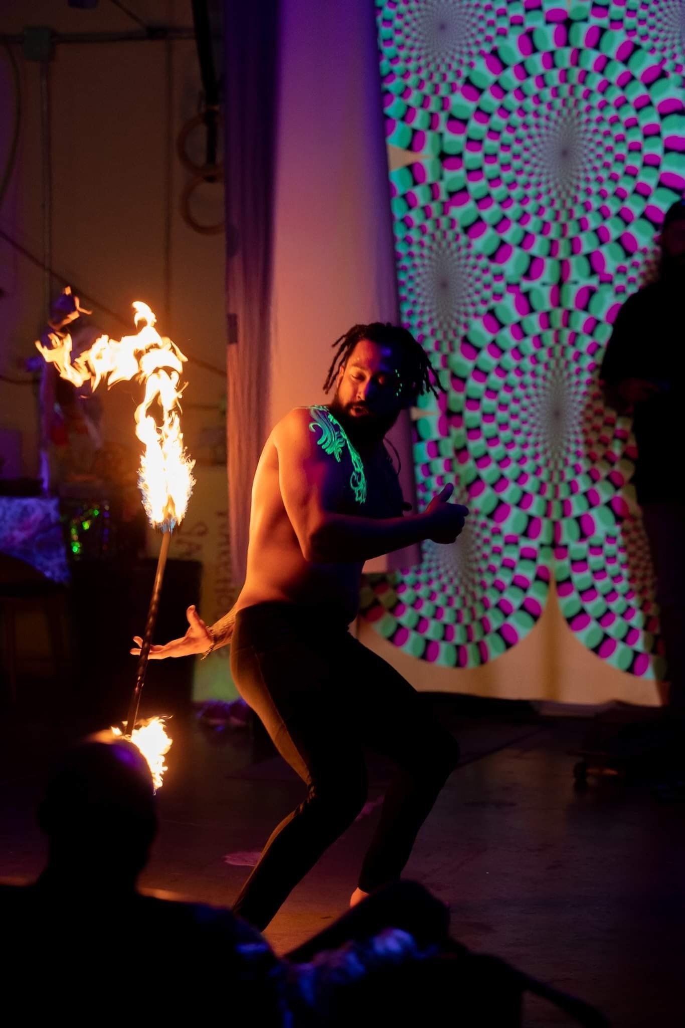A shirtless man is holding a fire stick in front of a glow in the dark wall.