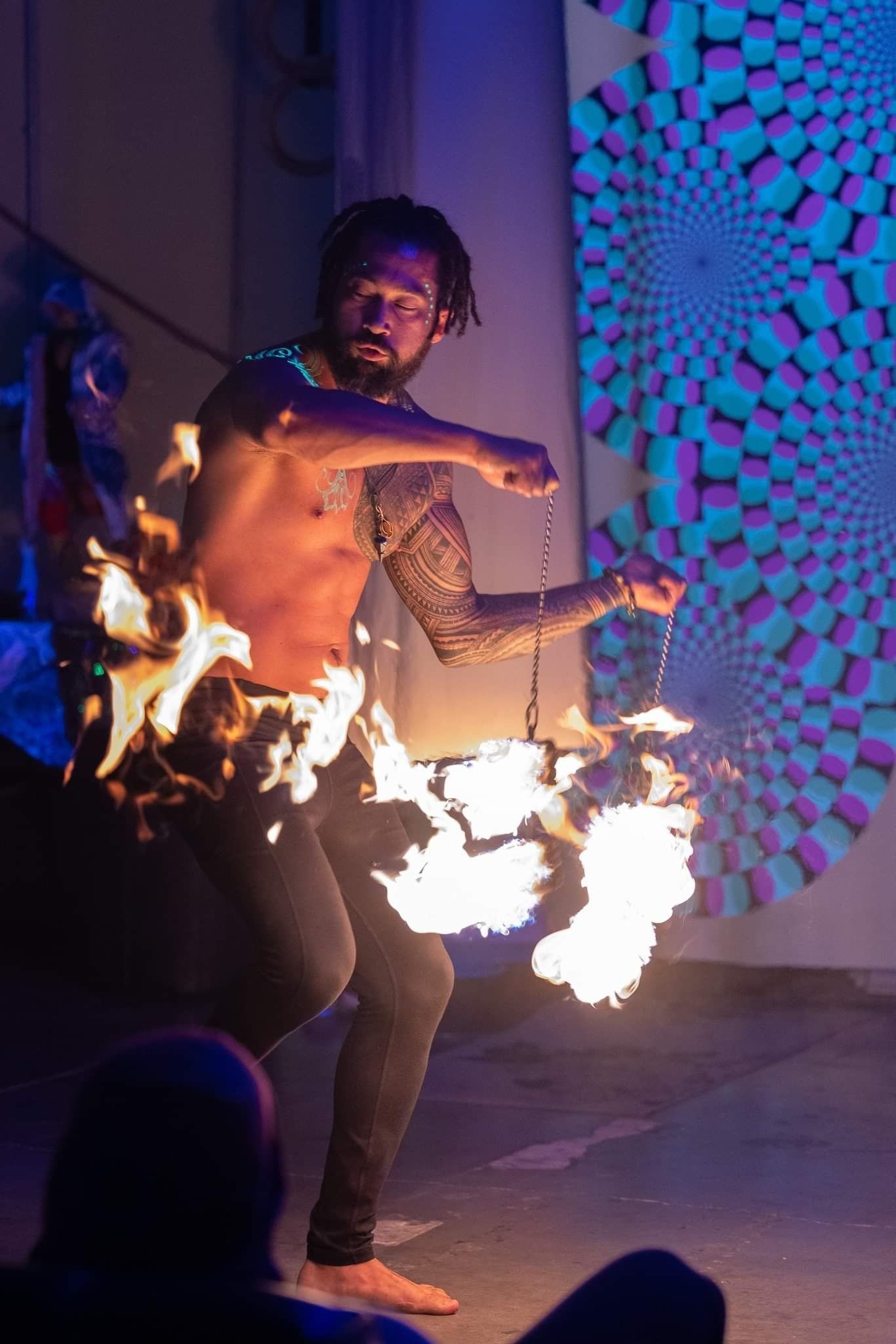 A shirtless man is holding a stick of fire in his hands.