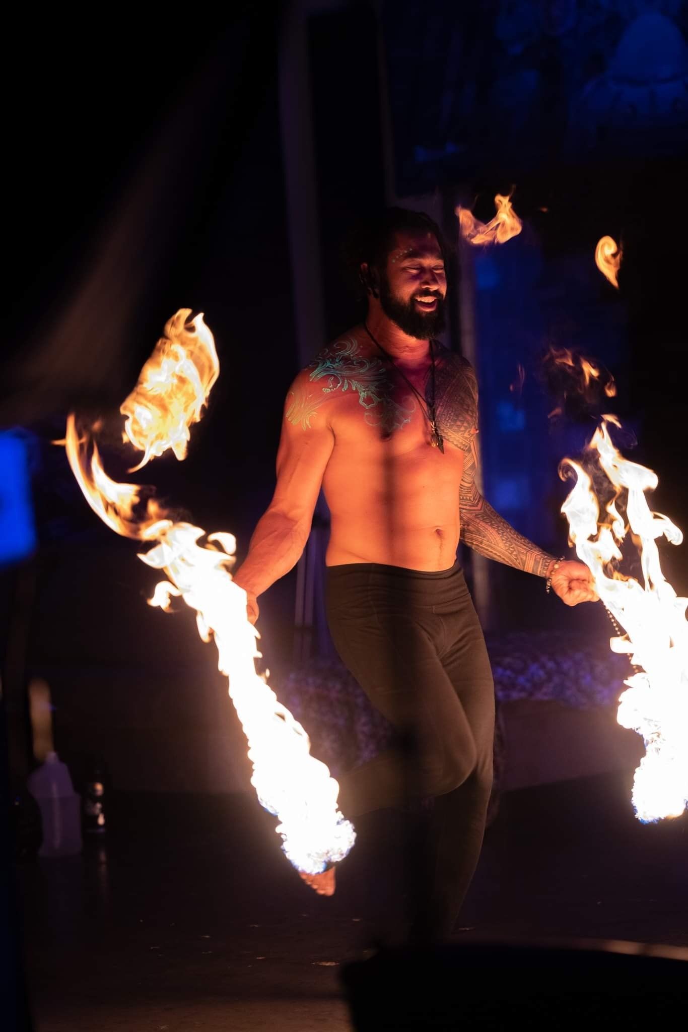 A shirtless man is holding two sticks of fire in his hands.