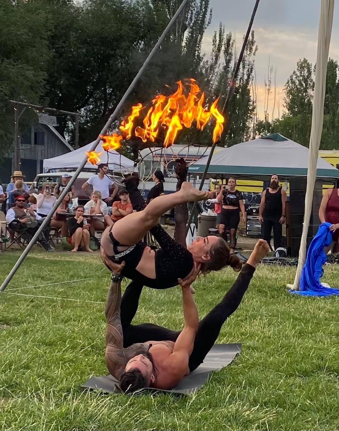 A man and a woman are performing aerial acrobatics with flames behind them.