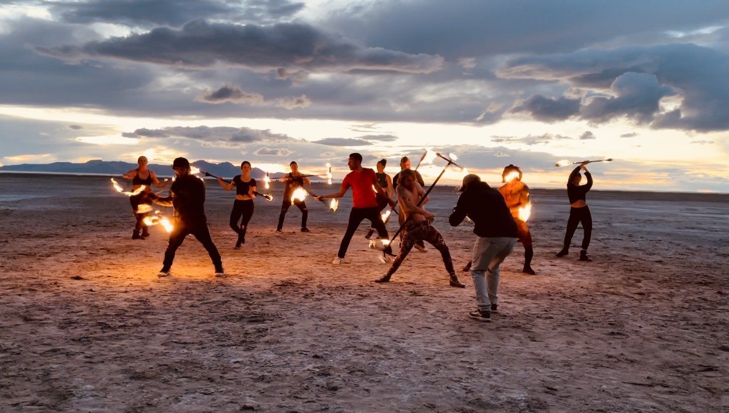 A group of people are standing on a beach holding fire.