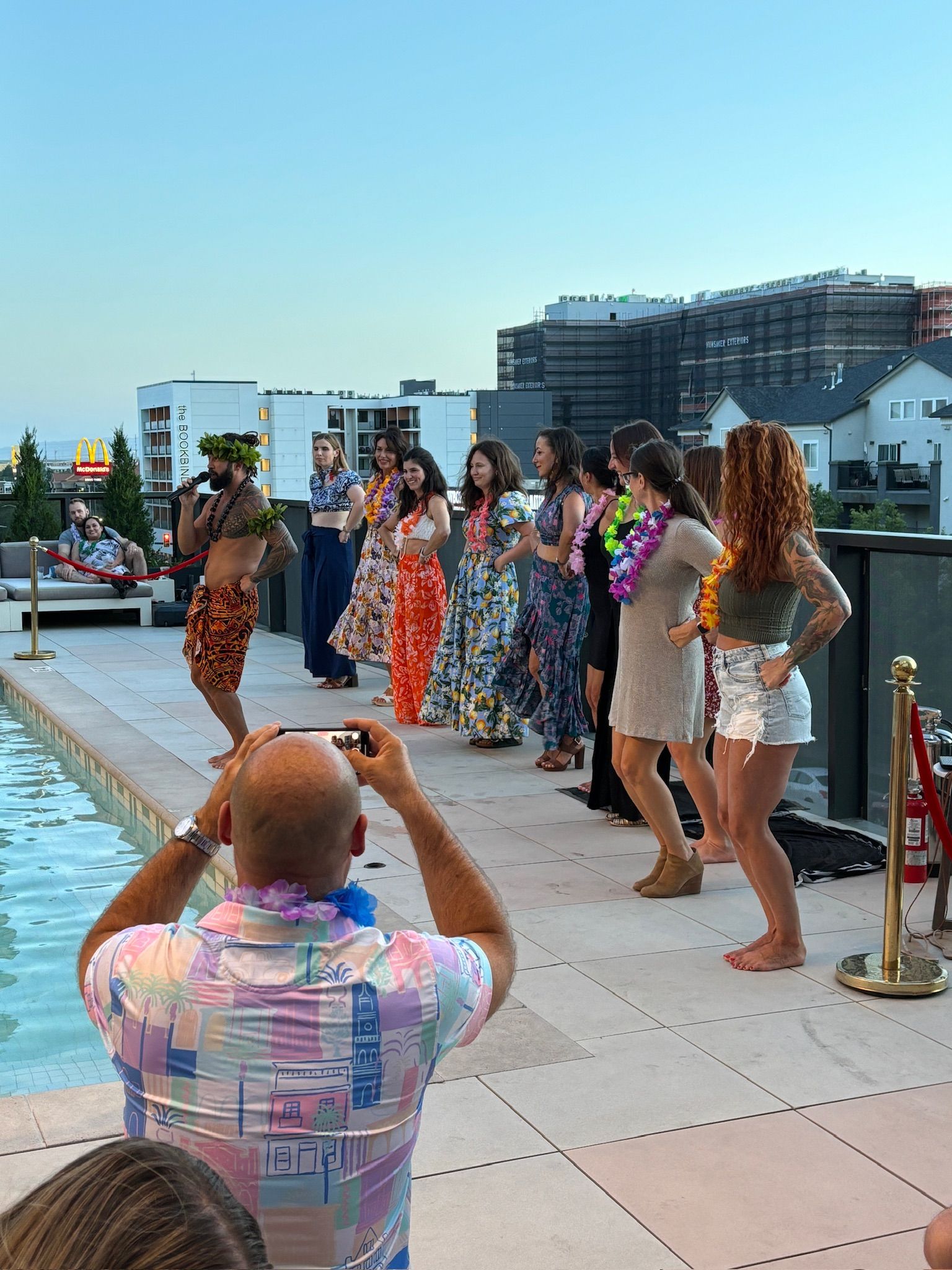 A man is taking a picture of a group of people dancing by a pool.