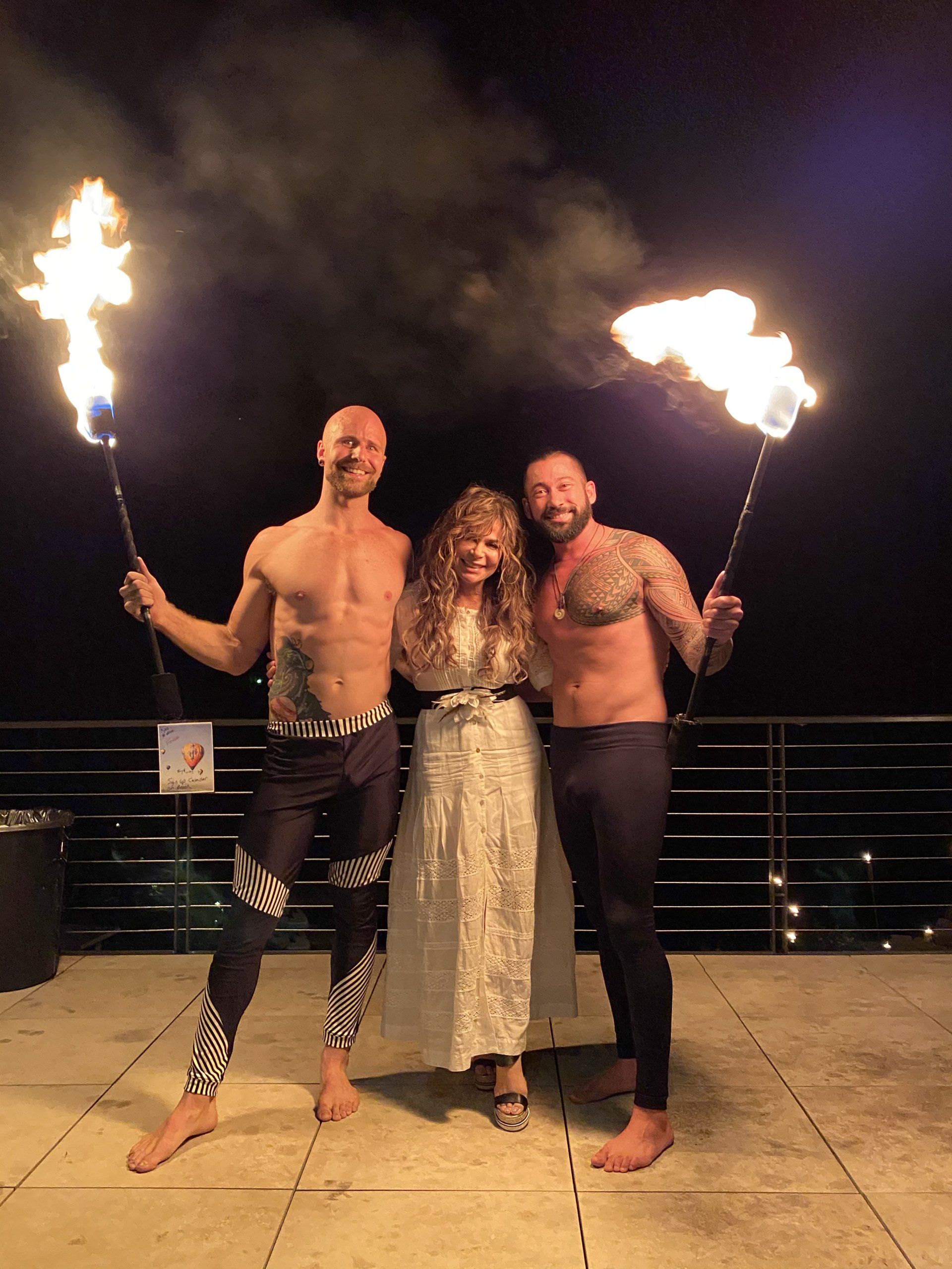 A bride and groom are posing for a picture with two men holding fire torches.