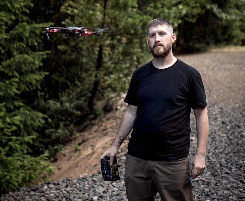 A man is holding a camera while a drone is flying in the background.