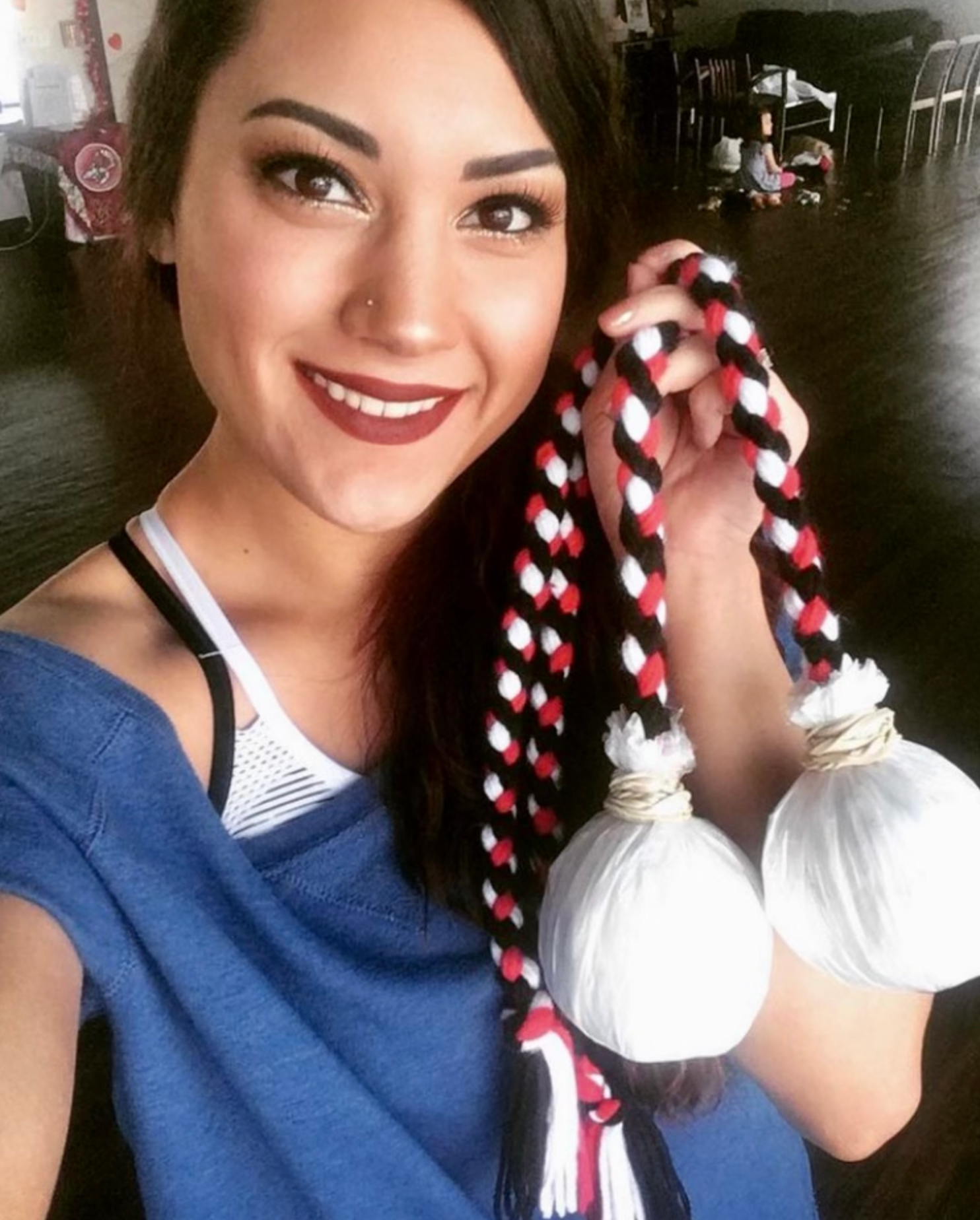 A woman in a blue shirt is smiling while holding two ropes