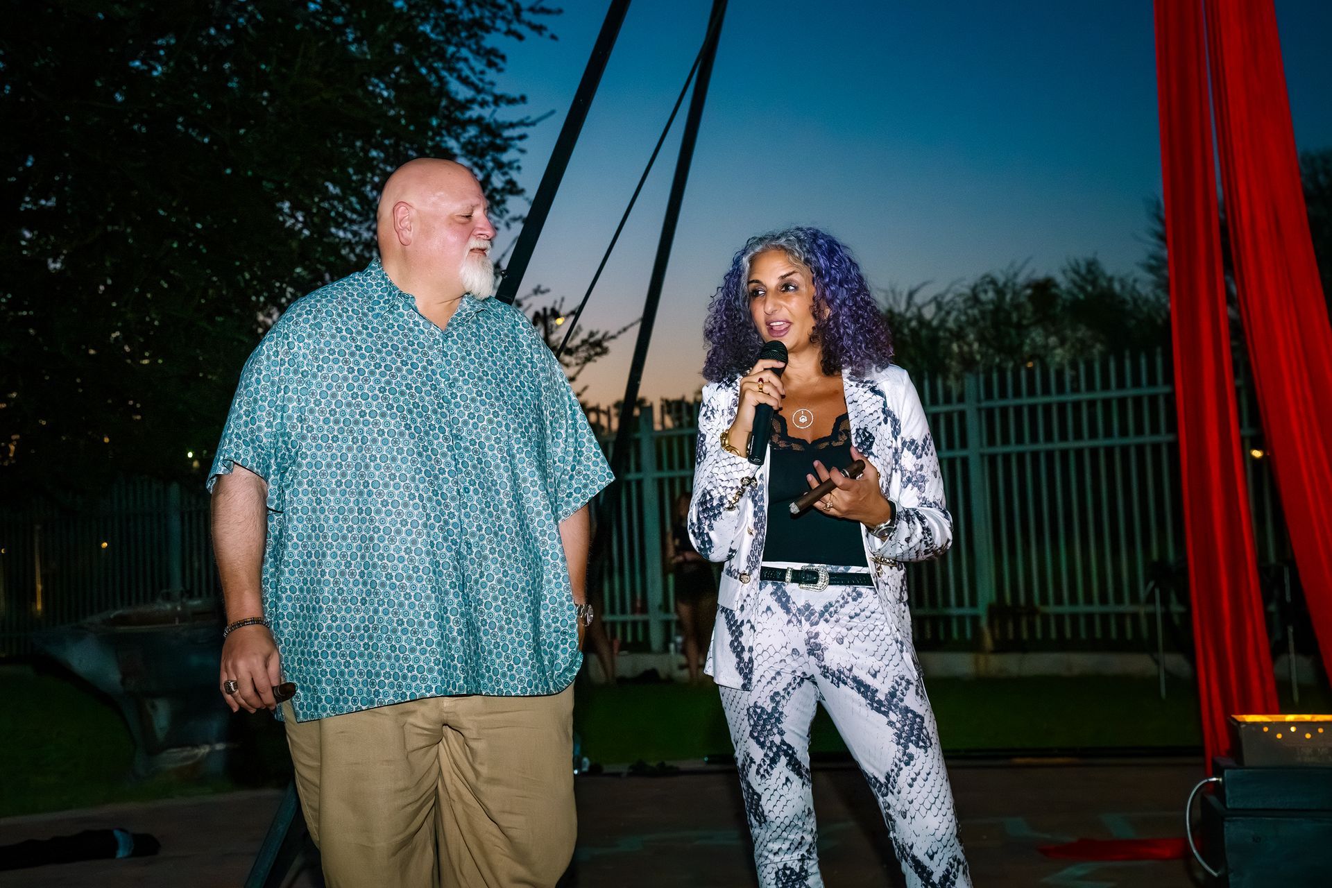 A man and a woman are standing next to each other talking into microphones.