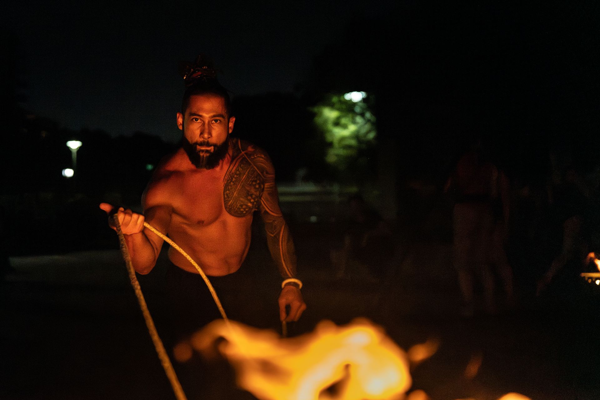 A shirtless man is jumping rope in front of a fire at night.
