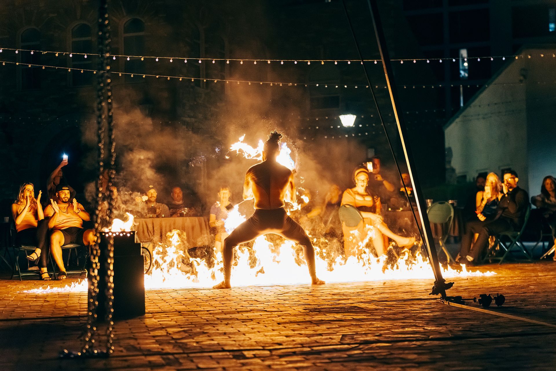 A man is standing in front of a large fire while people watch.