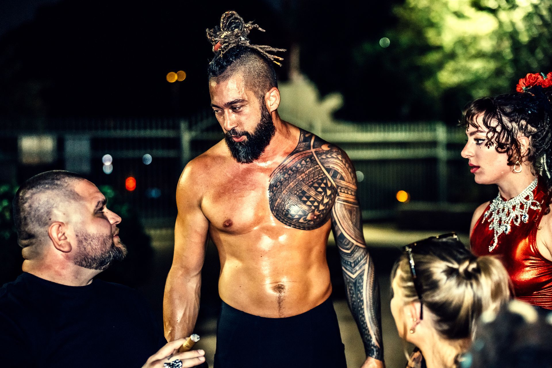 A shirtless man with a tattoo on his chest is standing next to a group of people.
