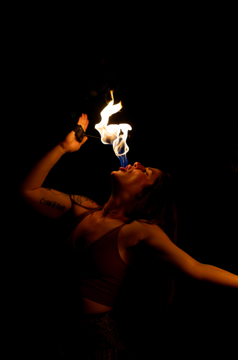 A woman is blowing fire from her mouth in the dark.