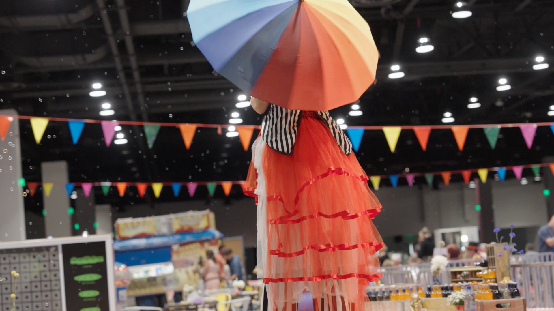 A woman on stilts holding a rainbow colored umbrella