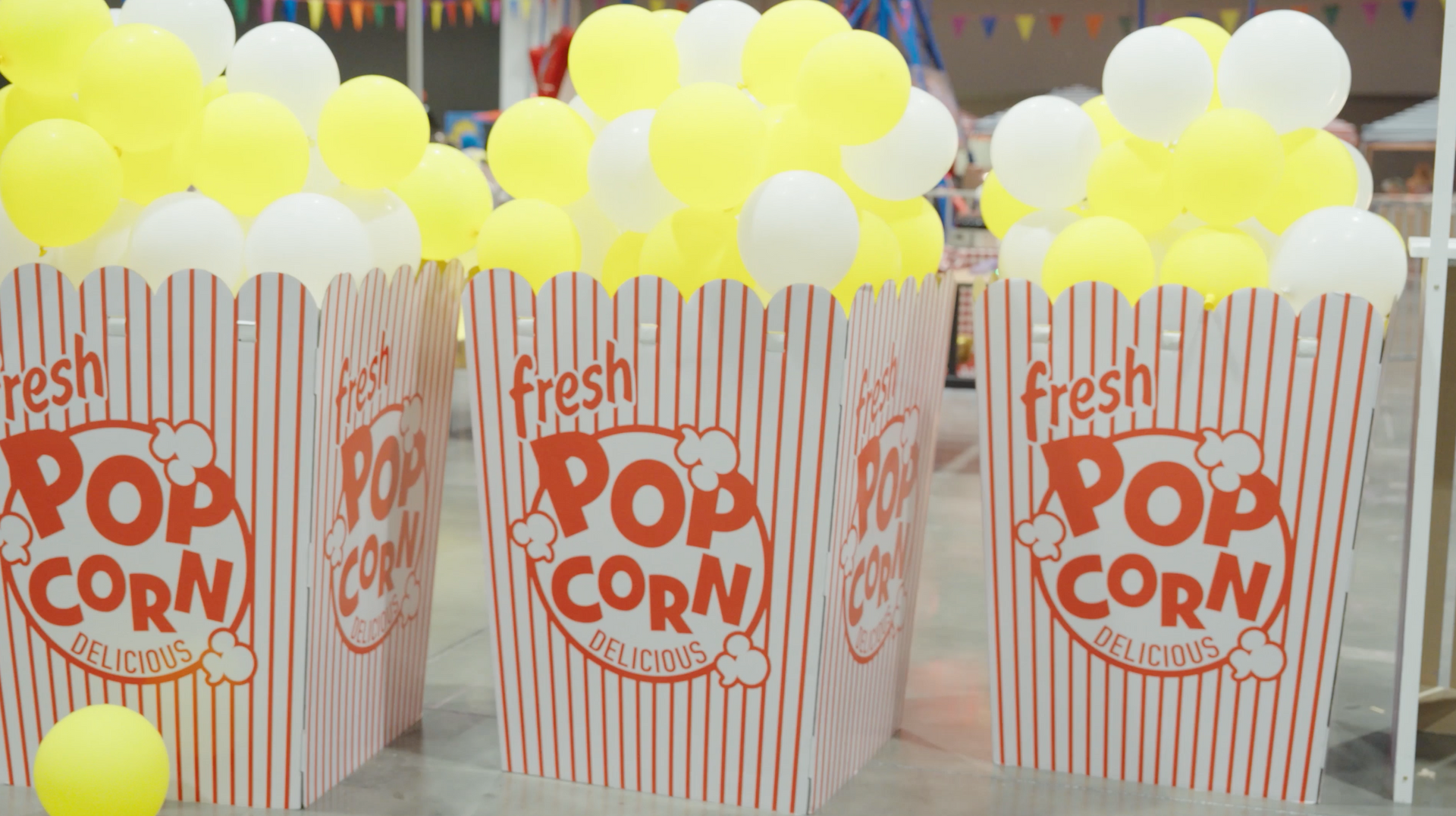 Three striped popcorn boxes filled with yellow and white balloons.