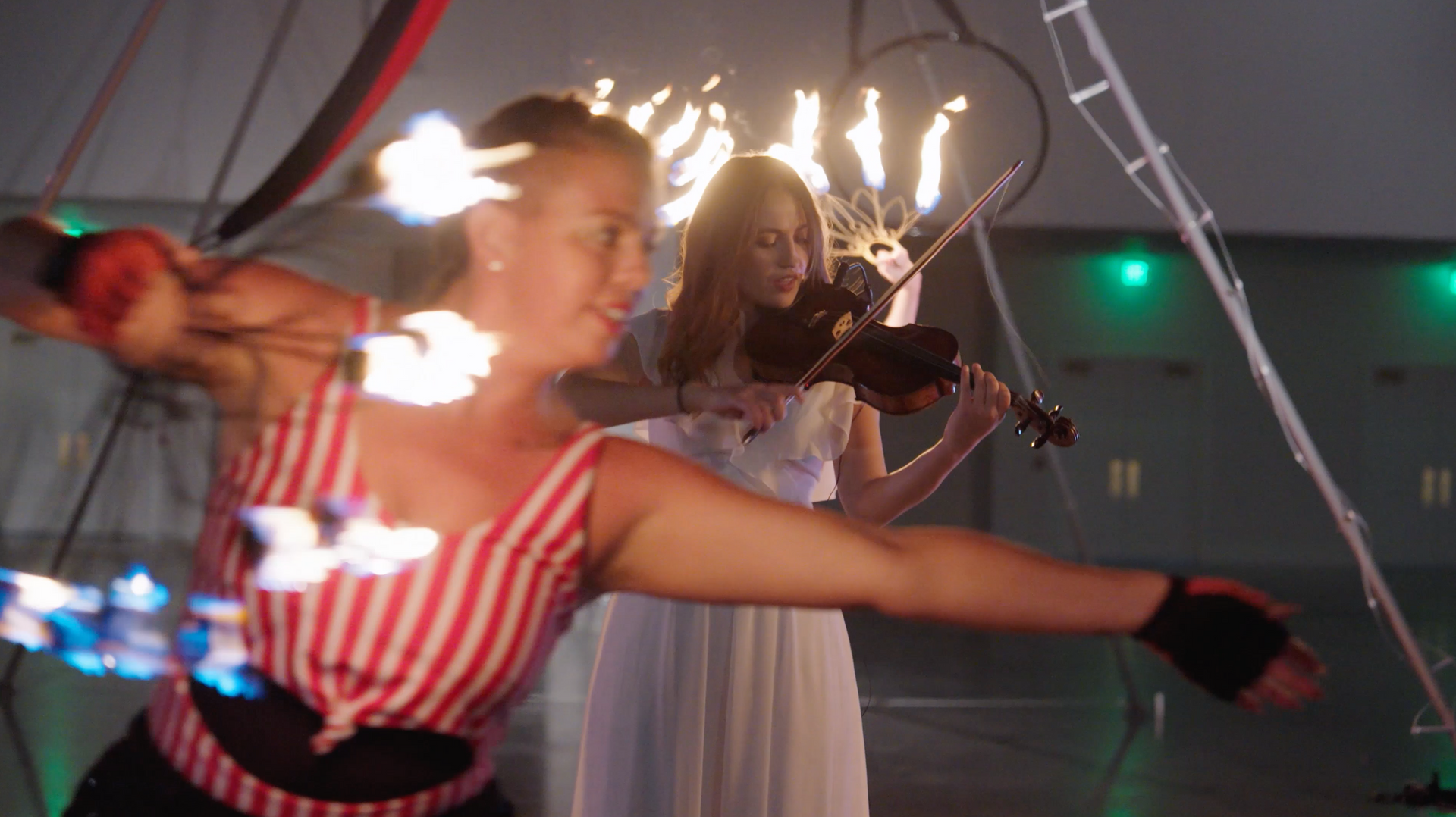 A woman is playing a violin while another woman is holding a fireball.